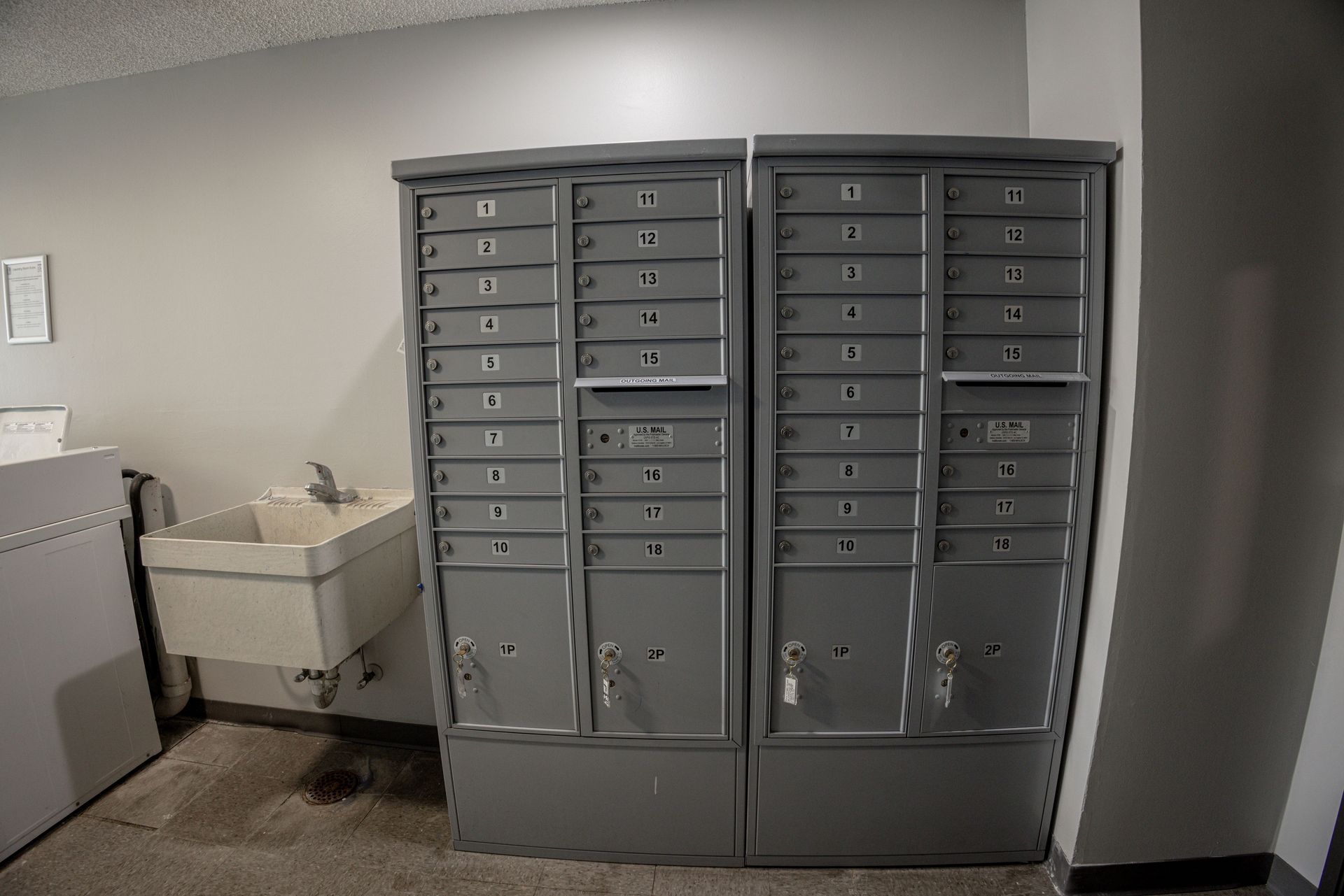 Row of gray apartment mailboxes beside a utility sink in a hallway