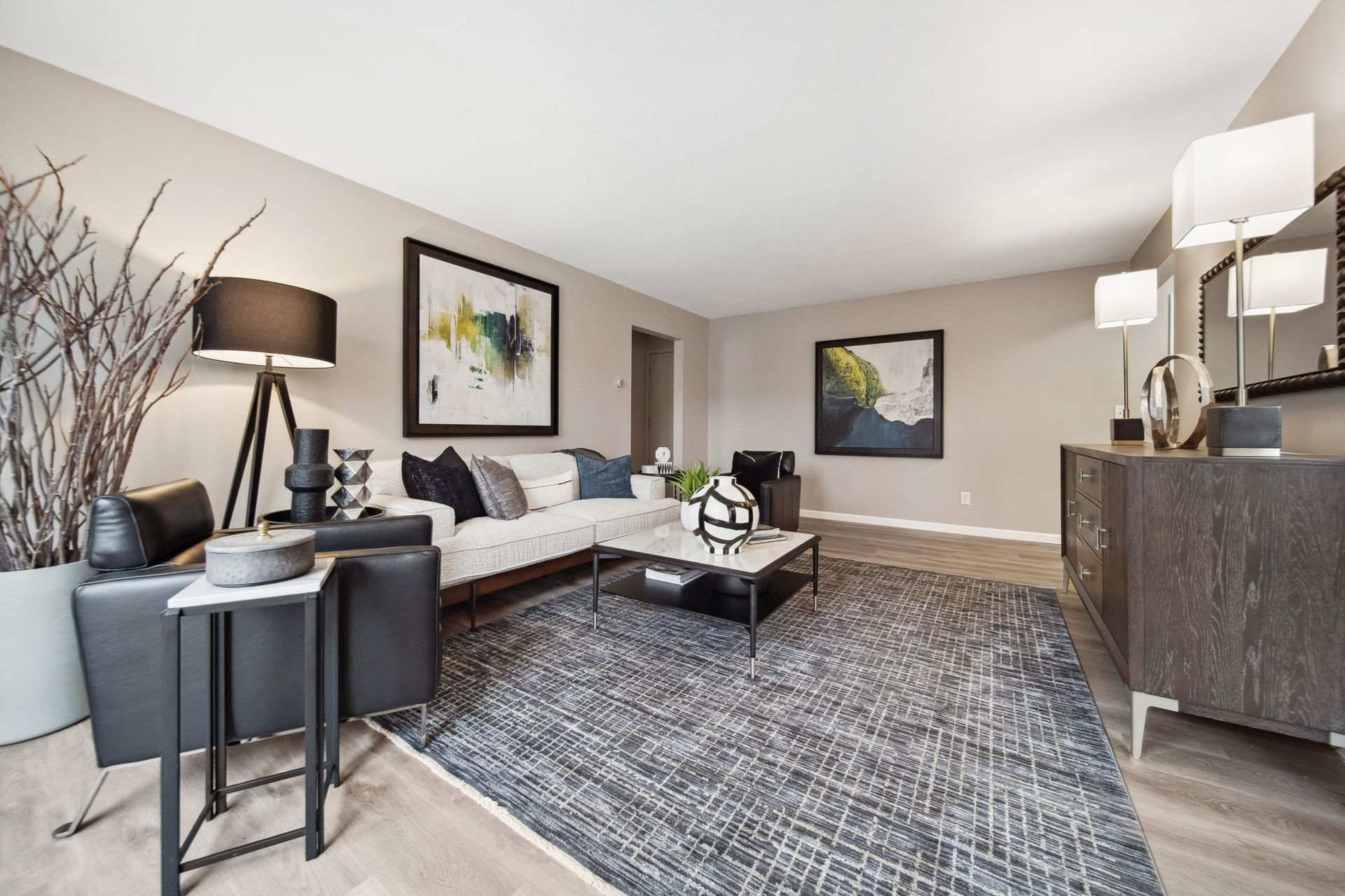 Modern living room with gray sofa, patterned rug, dark accent chairs, and wall art in neutral tones