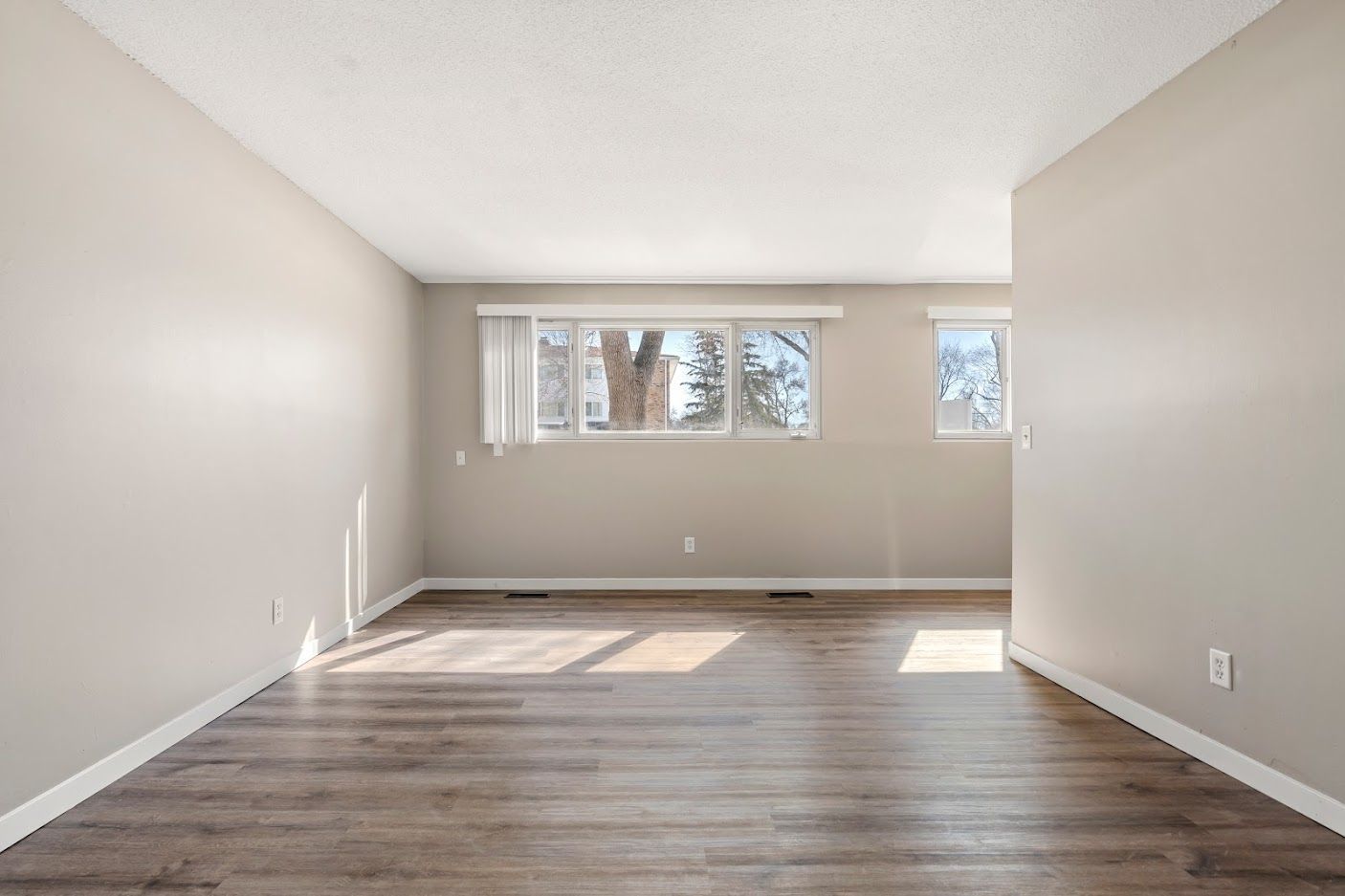 Empty living room with gray walls, wood flooring, and a wide window letting in daylight