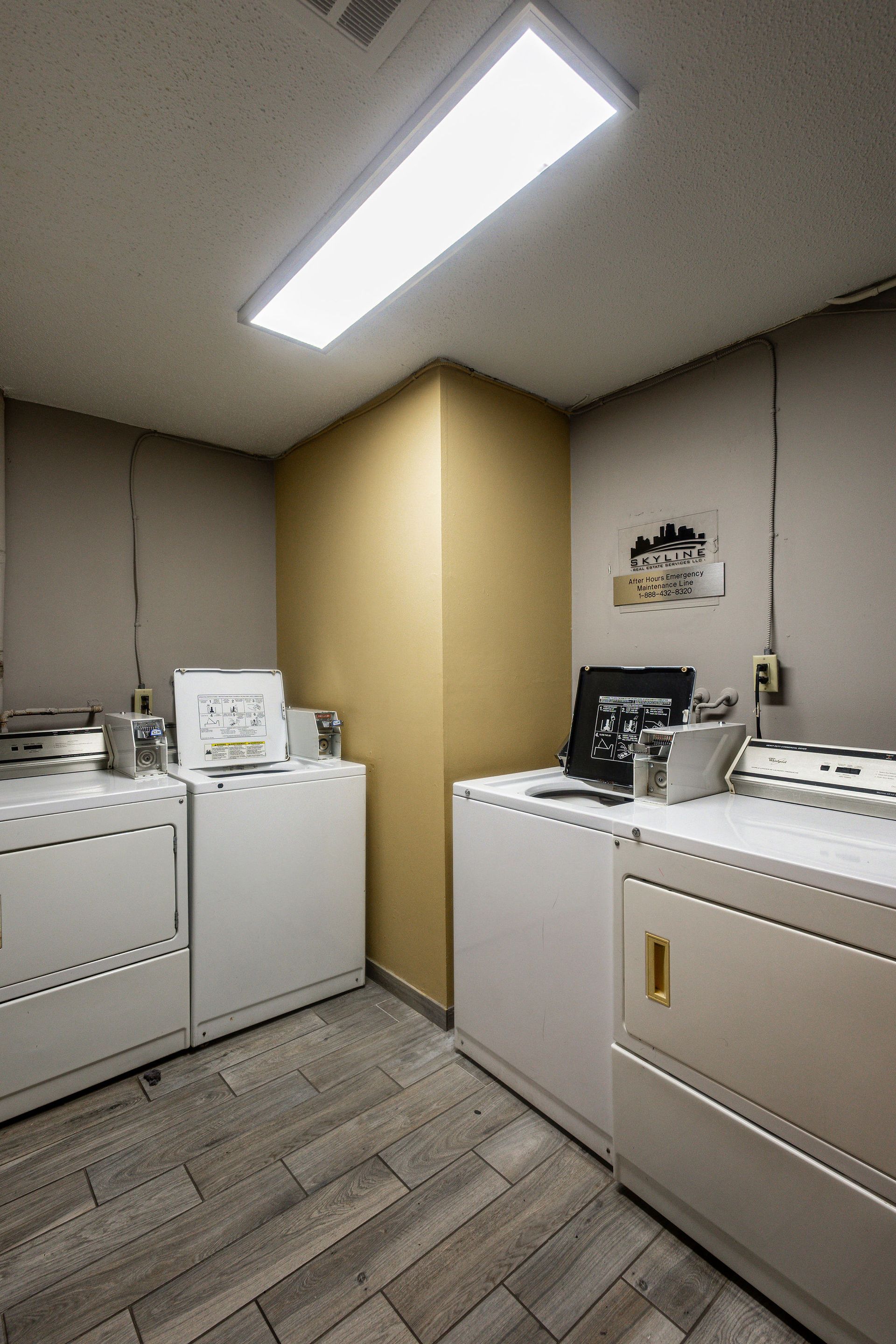 Laundry room with white washers and dryers under a bright ceiling light and beige walls