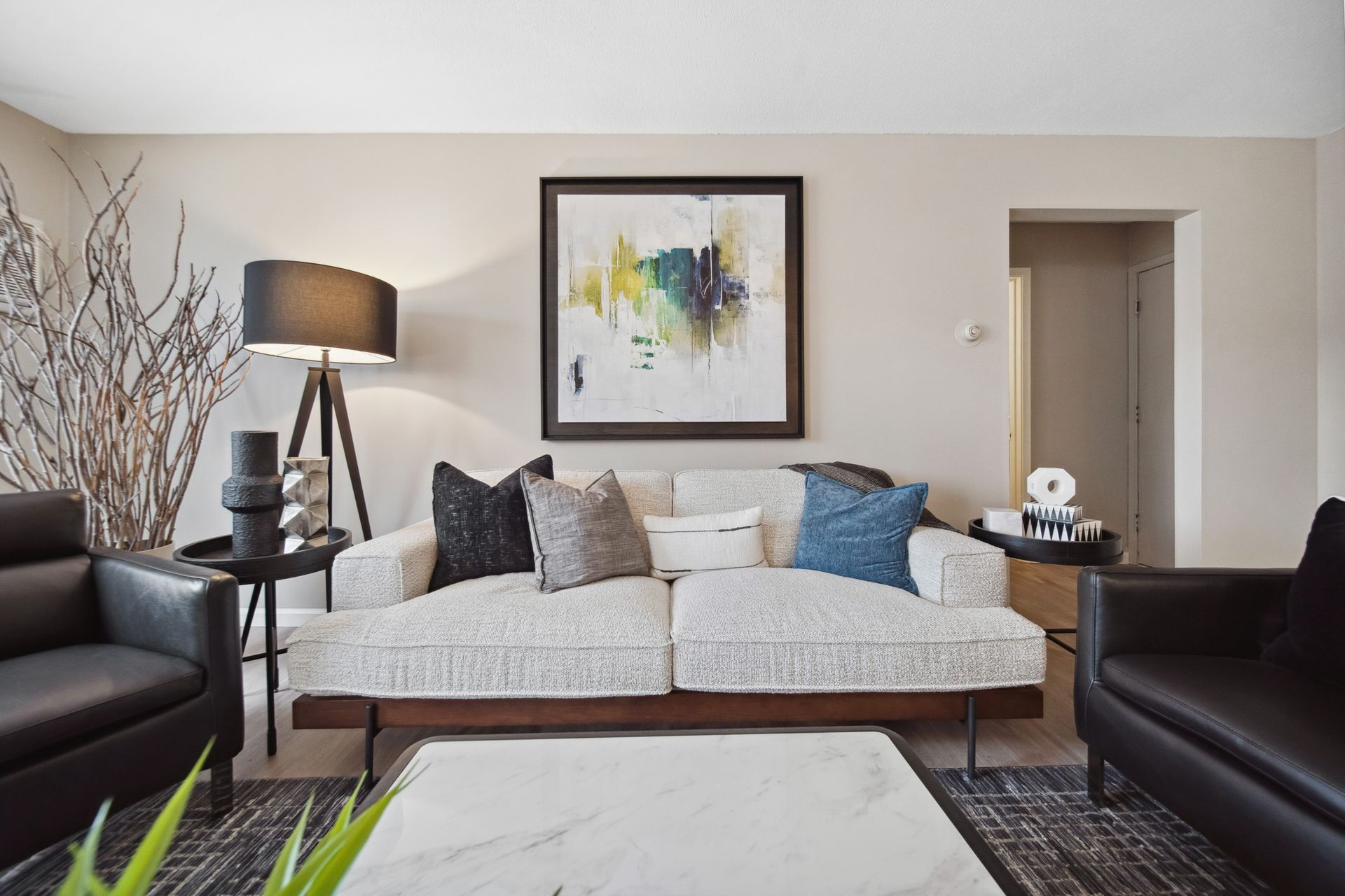 Modern living room with gray sofa, black armchairs, floor lamp, abstract wall art, and coffee table