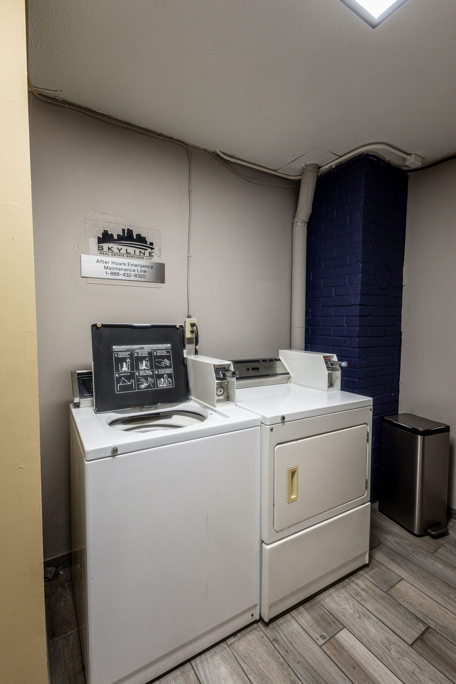 Laundry room with white washer and dryer, dark blue curtains, and a small trash bin in the corner.