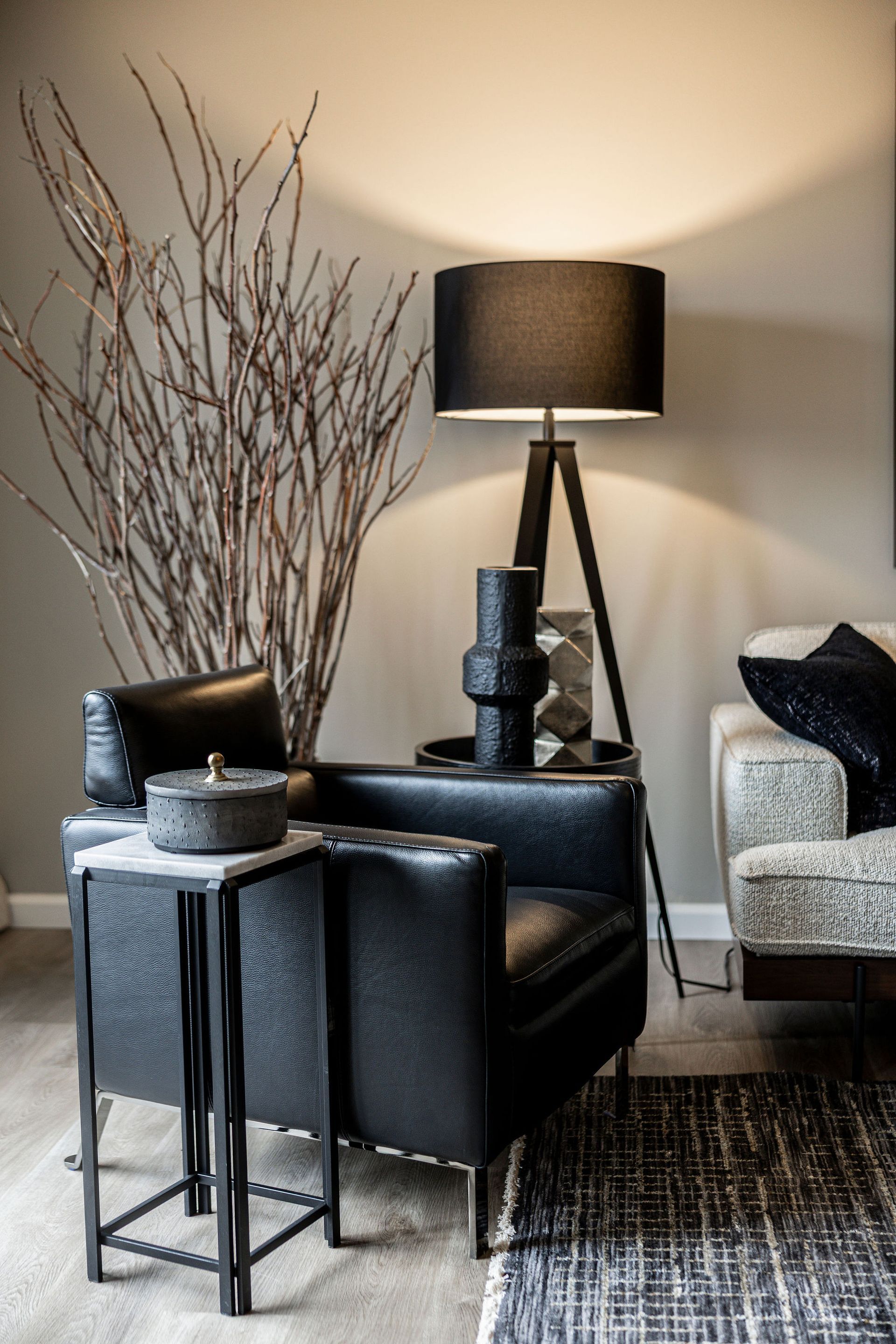 Cozy living room corner with black armchair, floor lamp, side table, and decorative branches