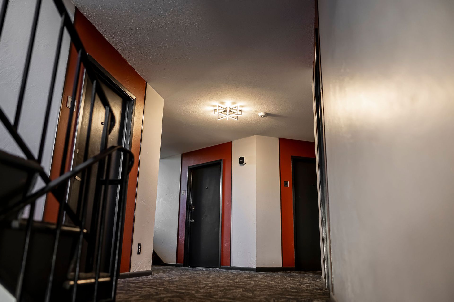 Hallway with orange and white walls, dark doors, and a staircase railing on the left