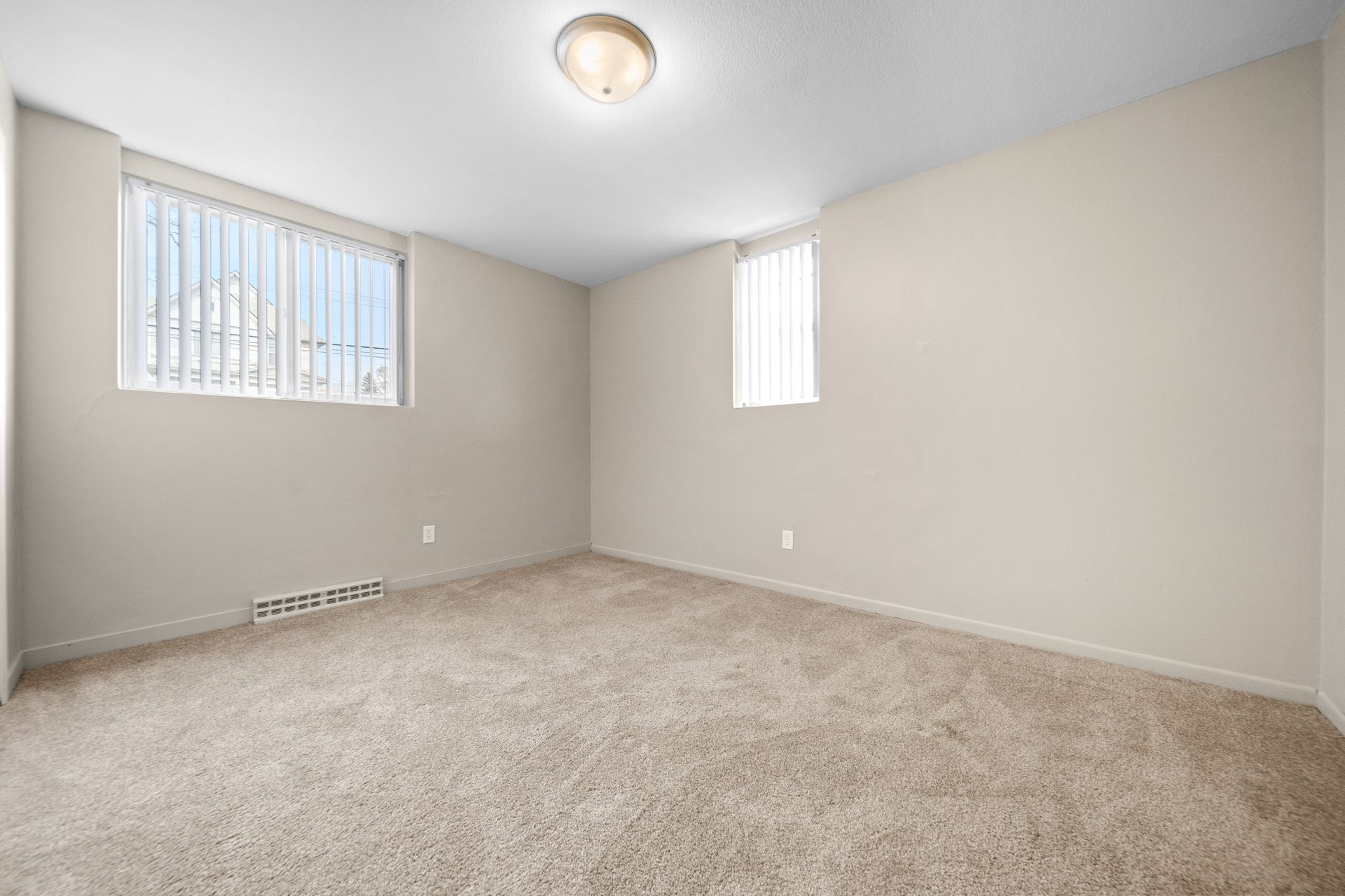Empty beige carpeted room with two small windows and a ceiling light