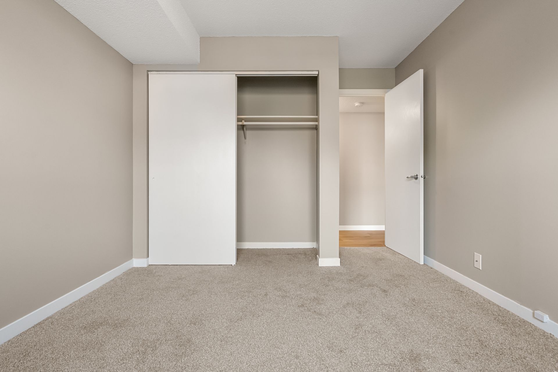 Empty beige bedroom with open closet and white door