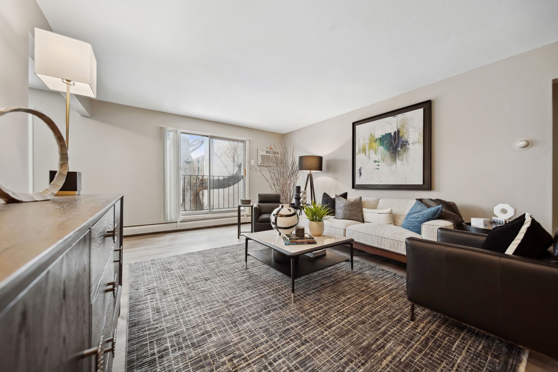 Modern living room with sofa, coffee table, patterned rug, artwork, and balcony doors