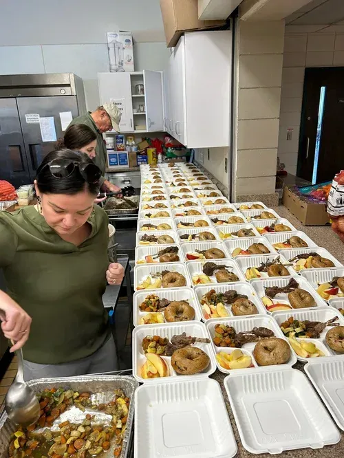 People packing rows of prepared meal trays in a kitchen