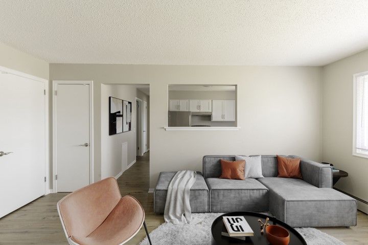 Bright living room with gray sectional sofa, tan chair, coffee table, and open view to kitchen.