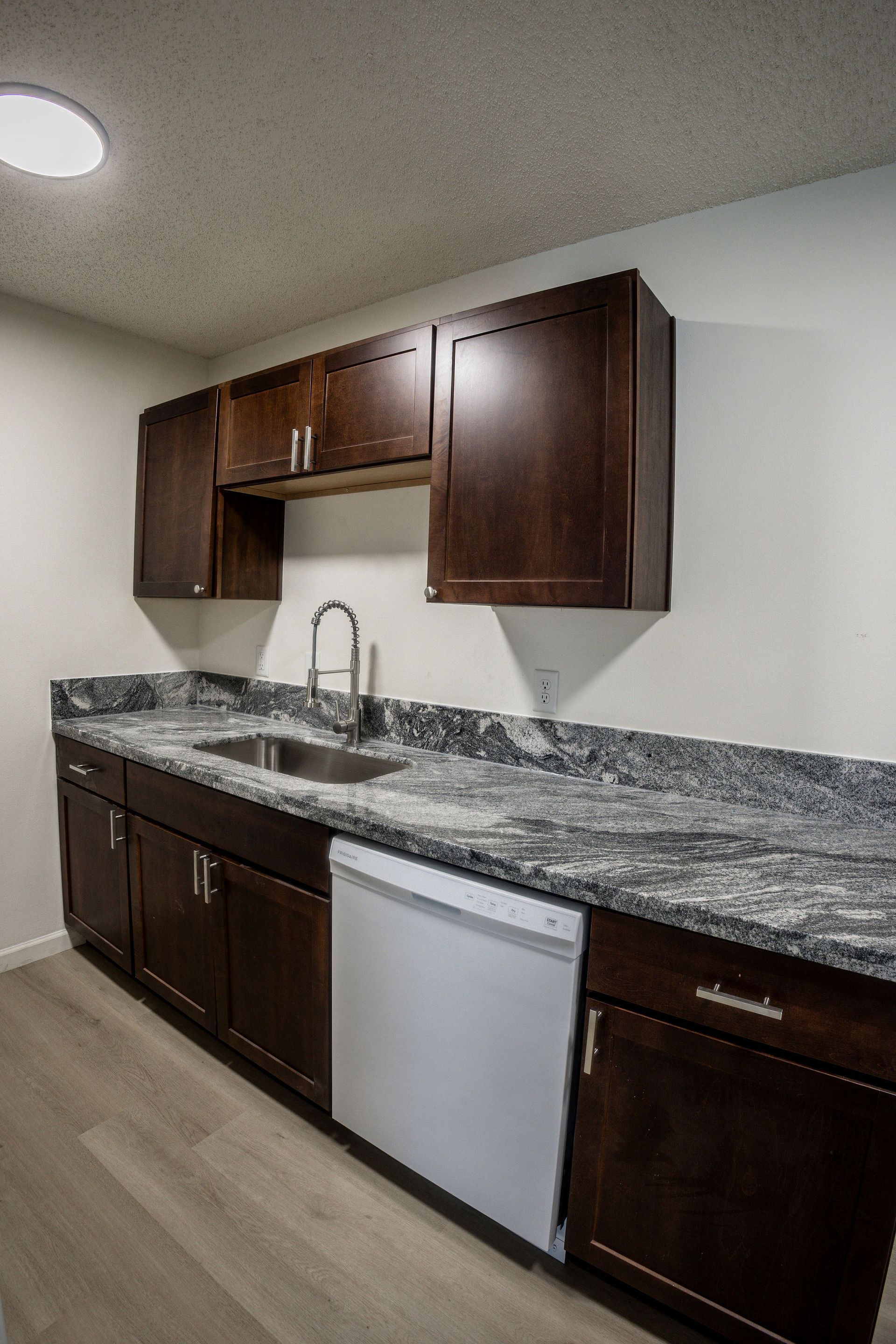 Small kitchen with dark wood cabinets, granite countertops, and a stainless sink and dishwasher.