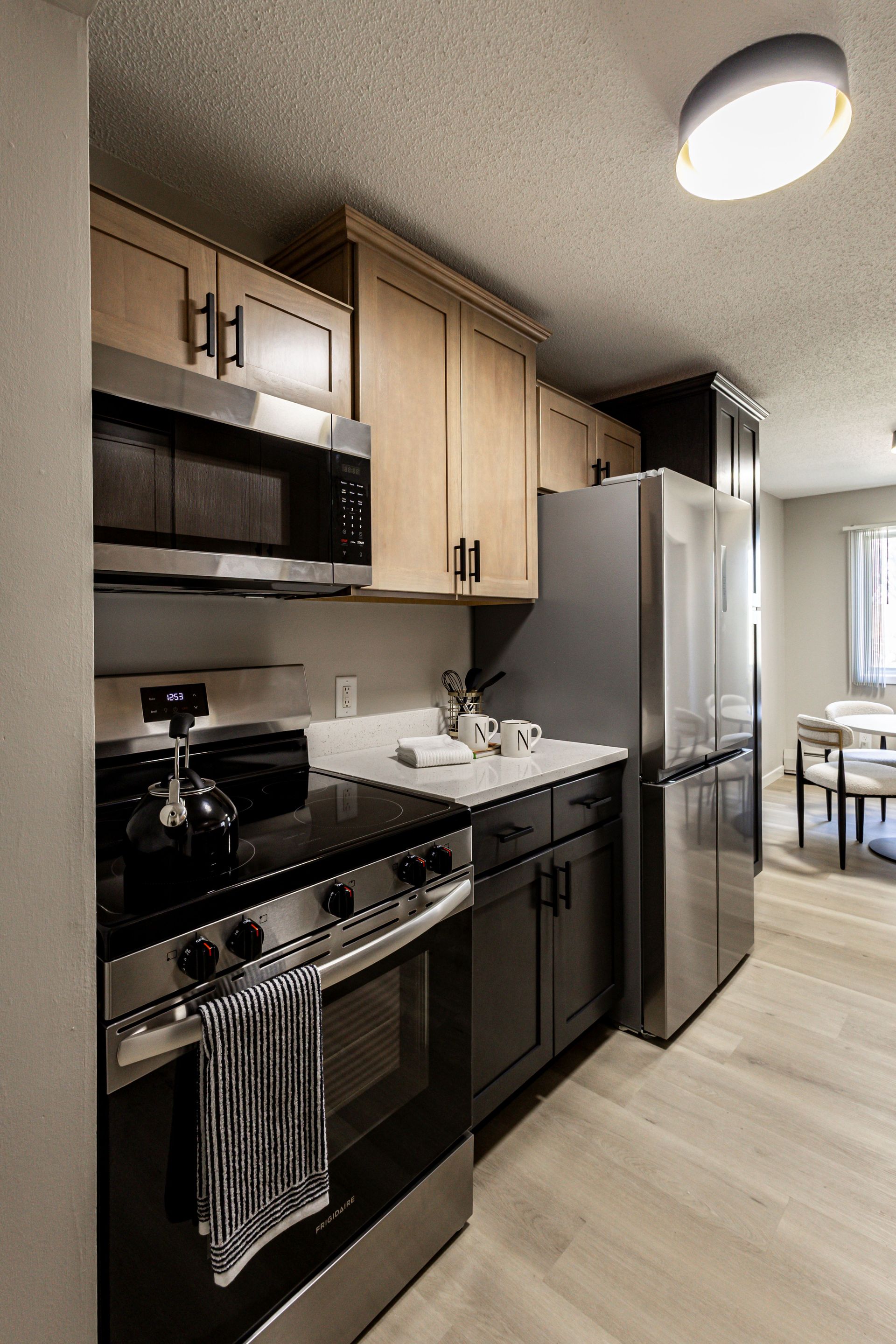 Modern kitchen with black appliances, light wood cabinets, stainless steel fridge, and dining area beyond