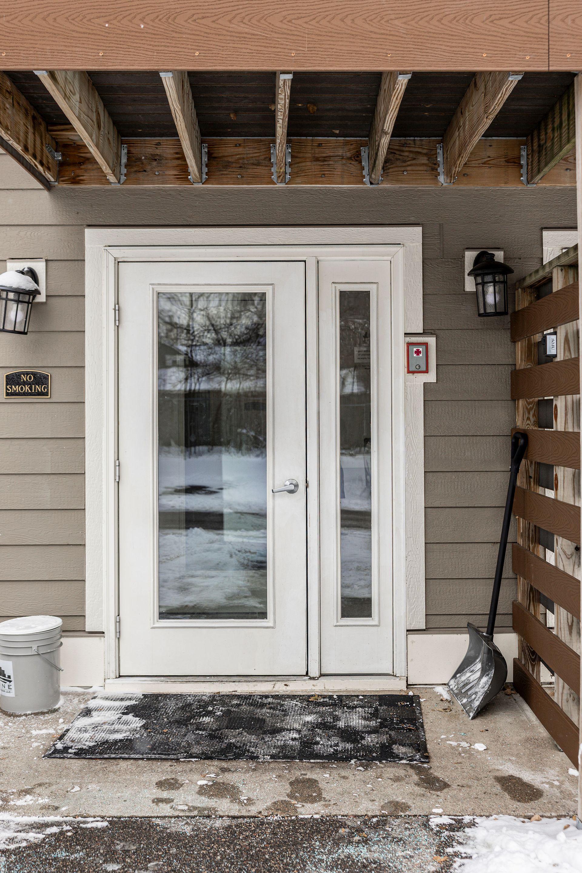 Snowy front porch with white double doors, stone siding, and wall lights under a covered entry