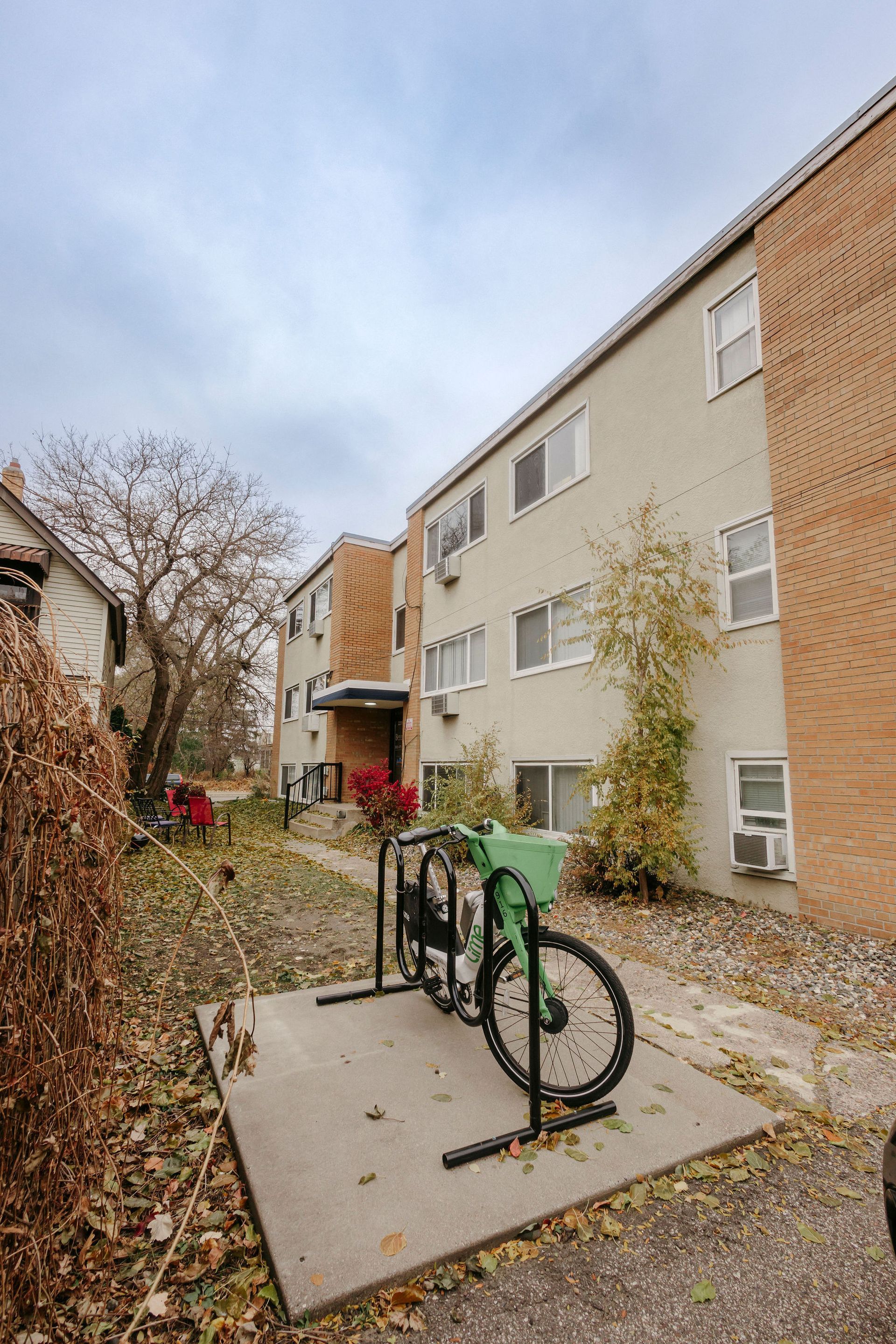 Apartment building courtyard with bike rack on a gravel path and leafless trees on an overcast day