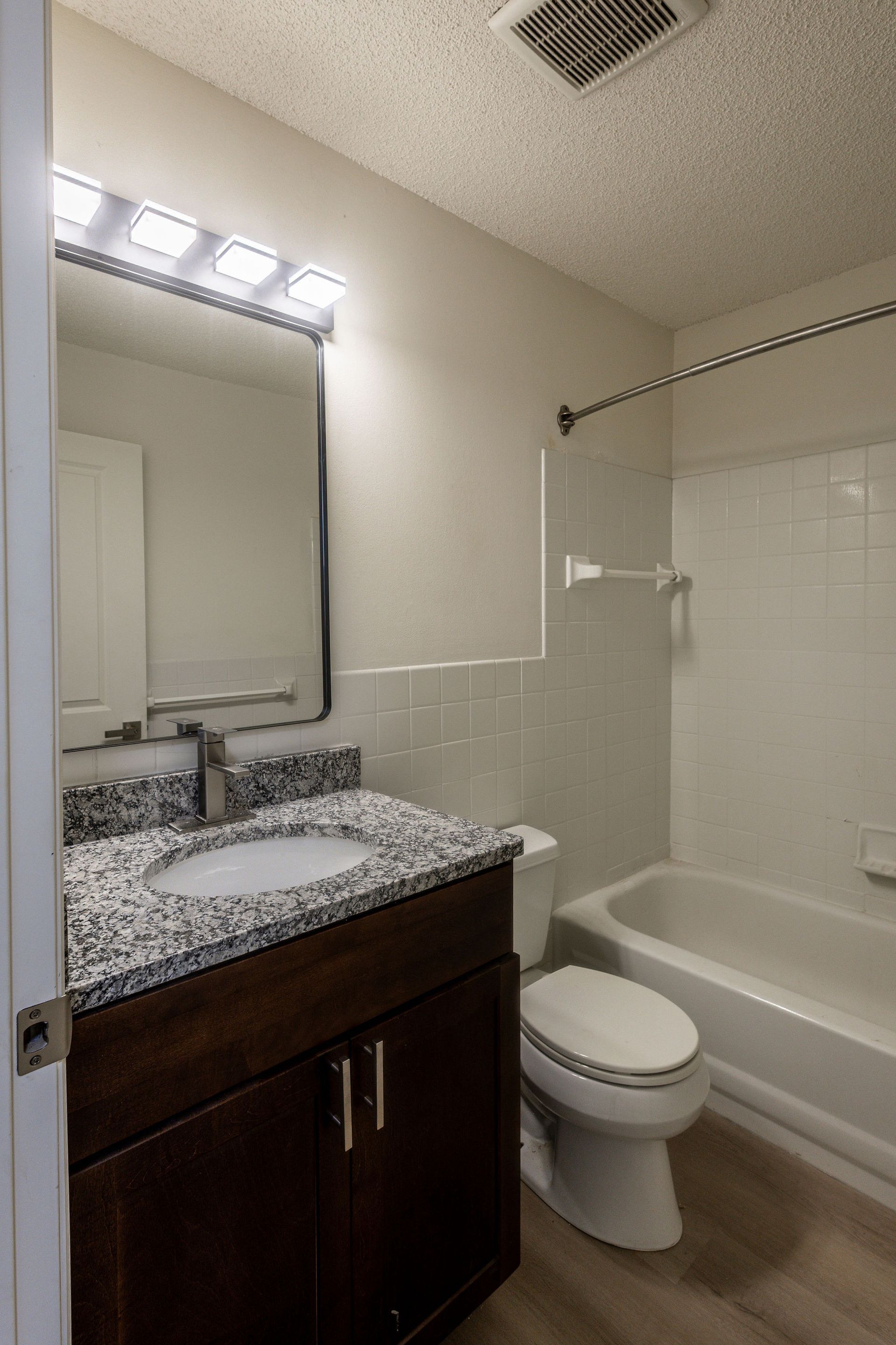 Small bathroom with dark vanity, granite countertop, mirror lights, toilet, and bathtub-shower combo.