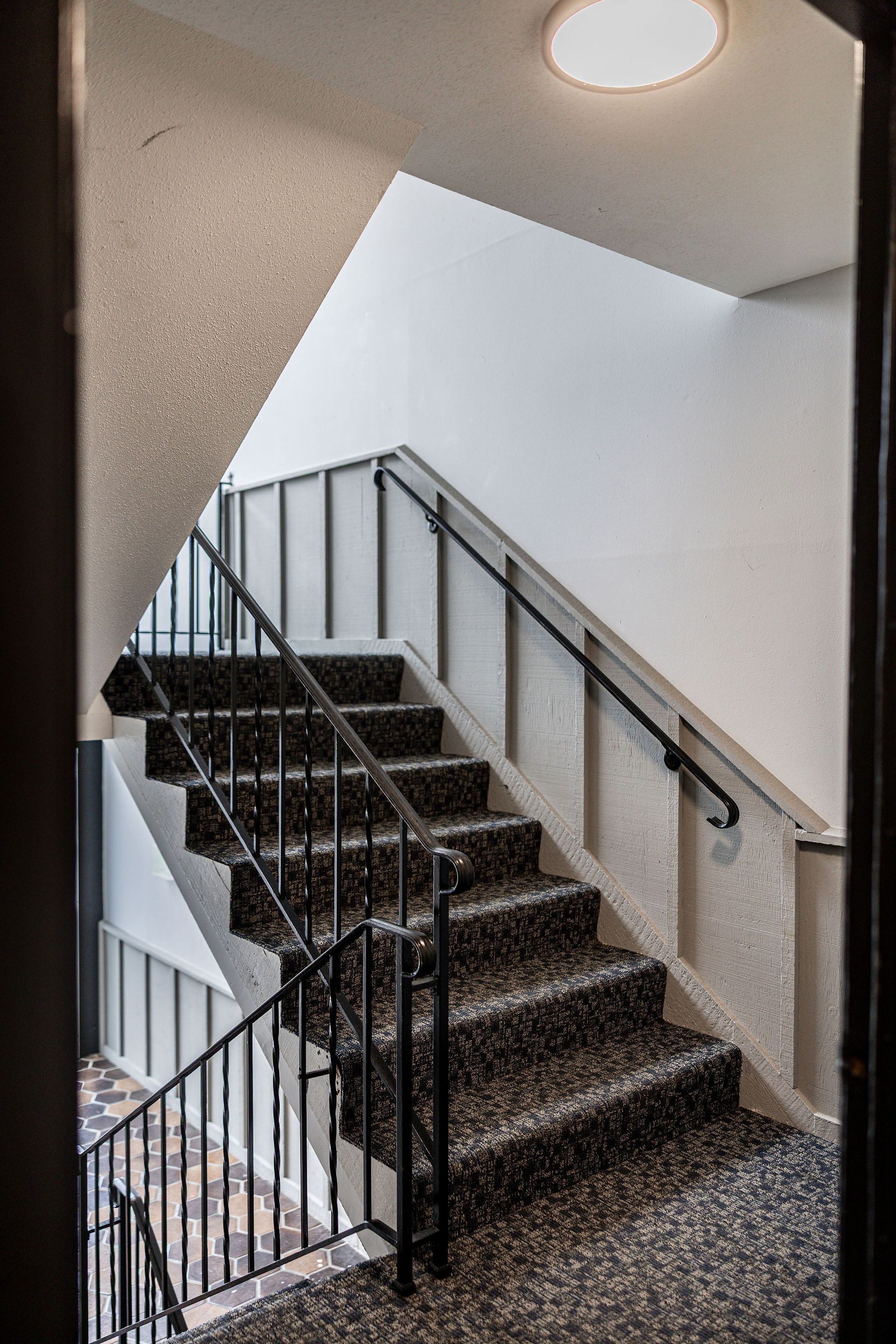 Indoor stairwell with black steps, white walls, and metal railings under a ceiling light