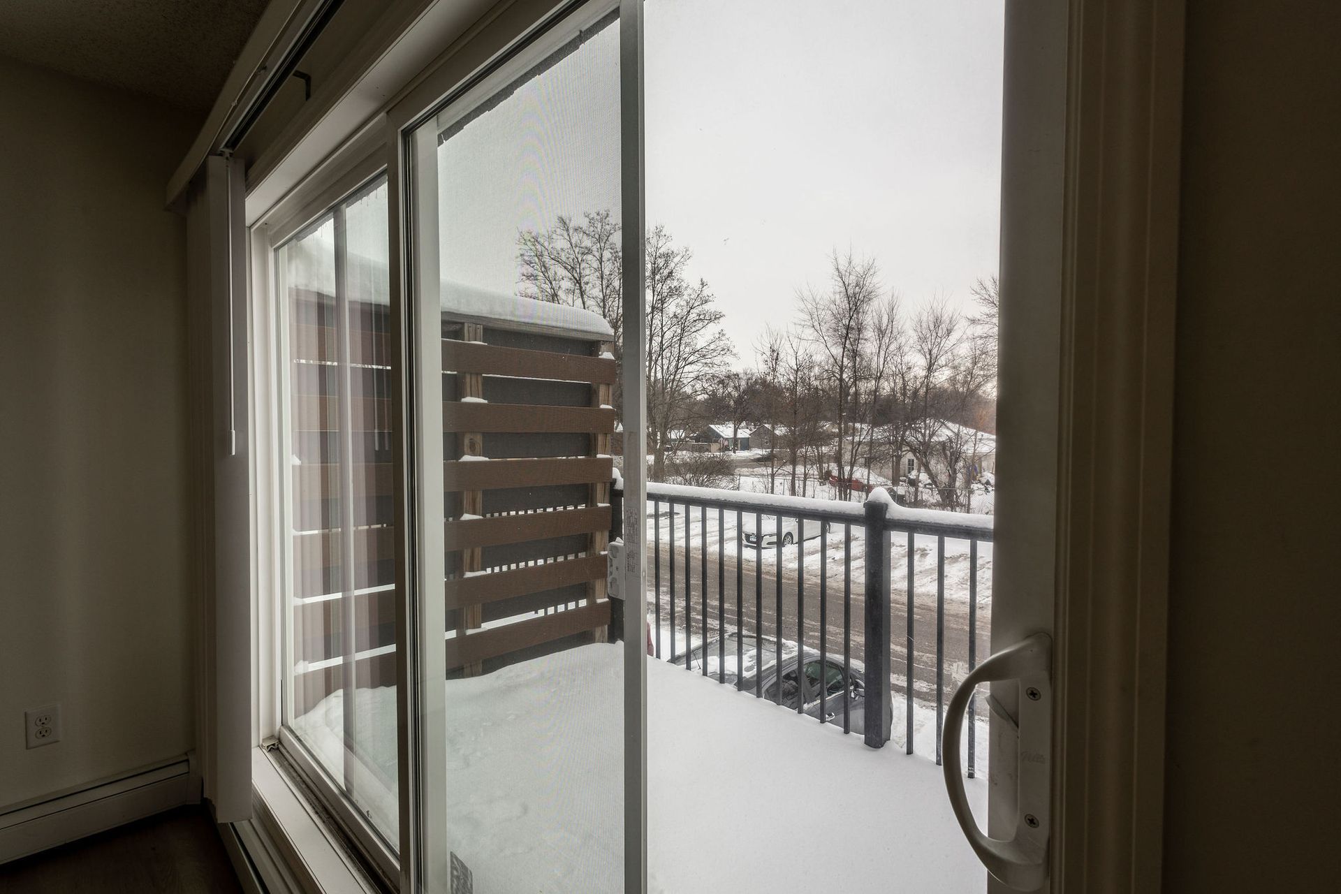 Sliding glass door to a snowy balcony with railing and nearby trees