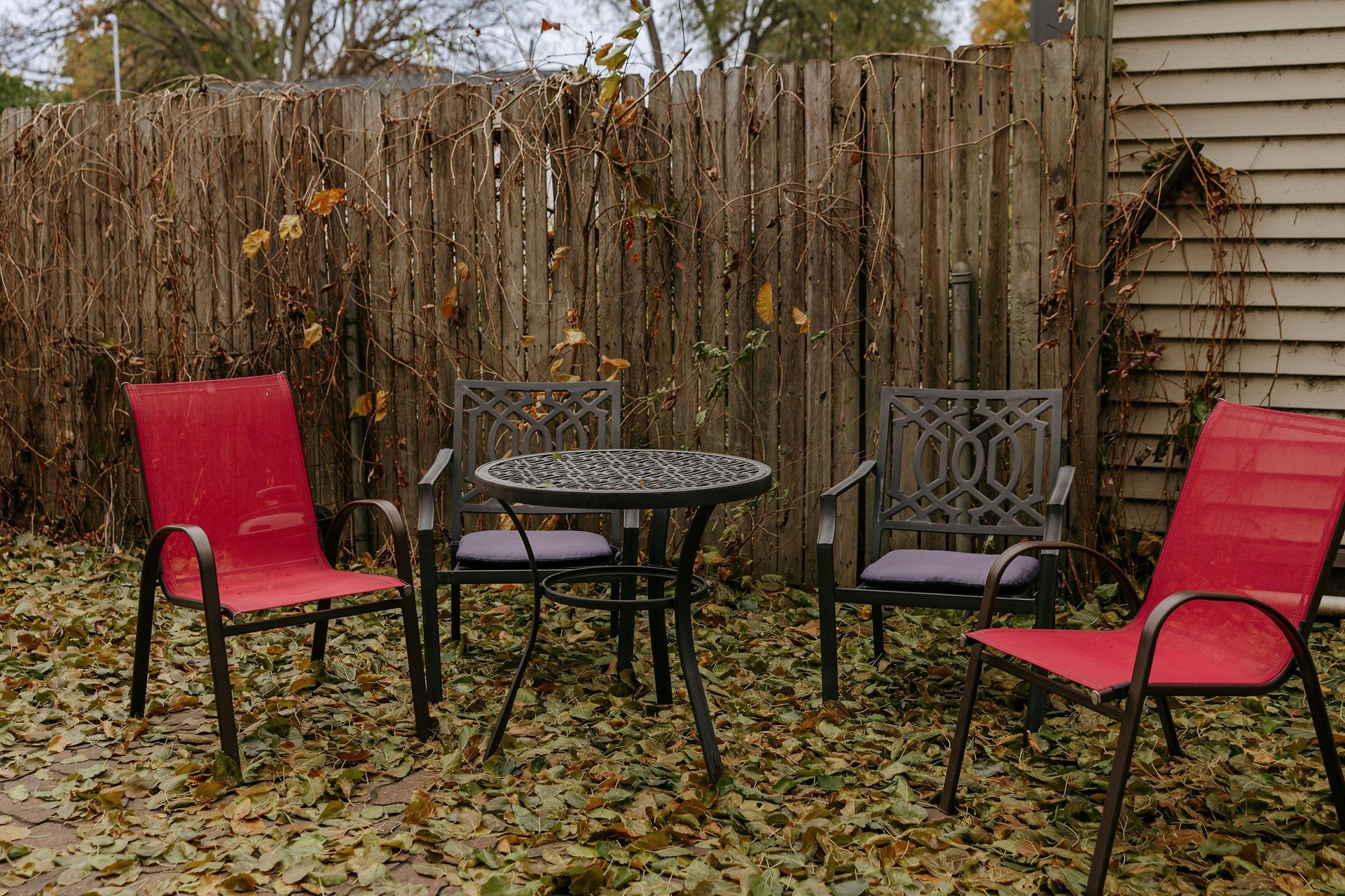 Outdoor patio with red and gray chairs around a black metal table in front of a wooden fence