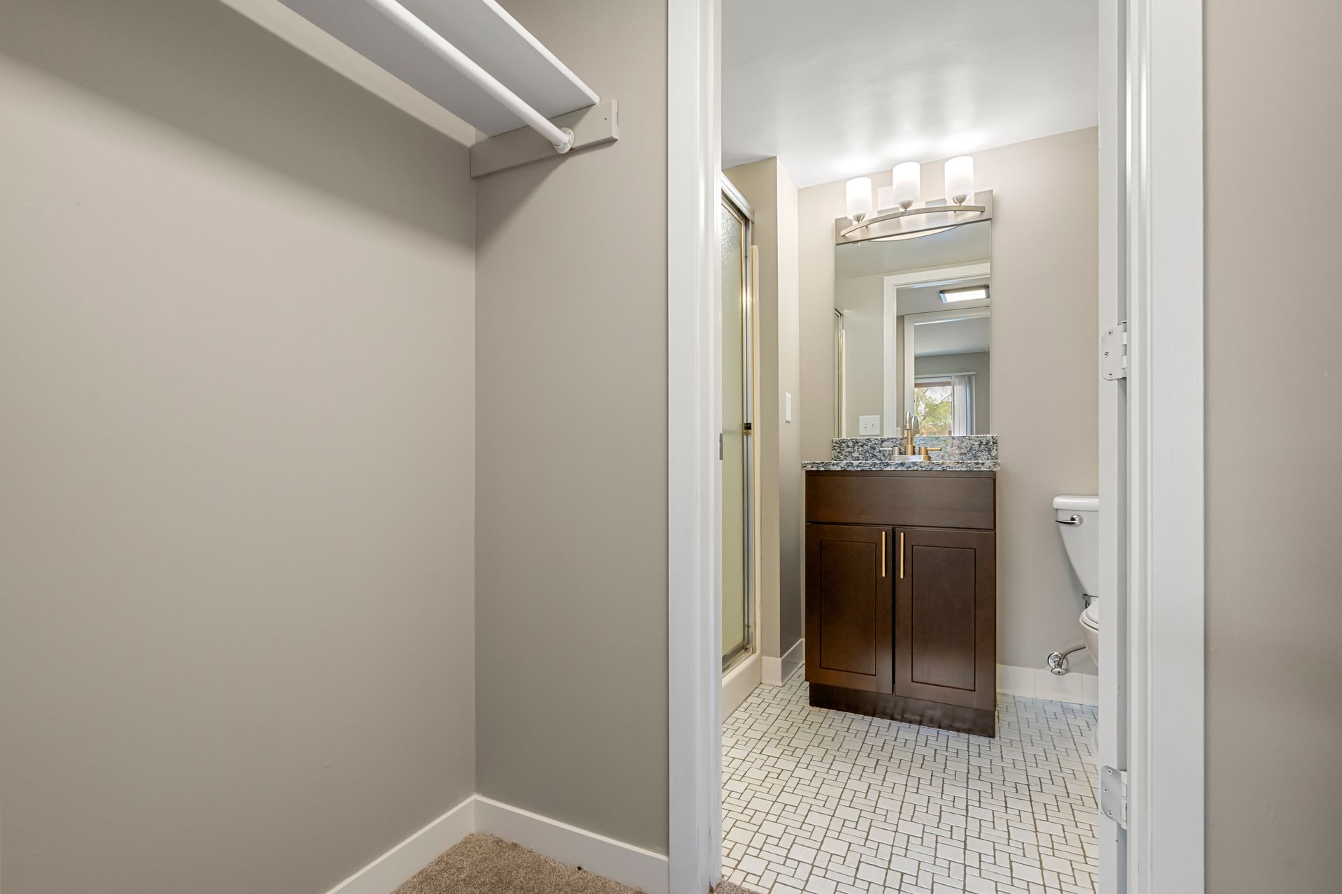 Narrow hallway leading to a small bathroom vanity with mirror and speckled tile floor