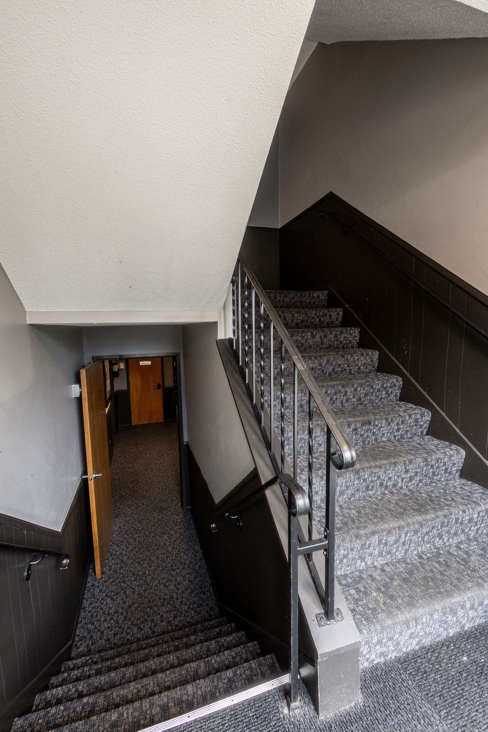 Indoor stairwell with gray carpeted stairs, black railings, and an open door at the landing