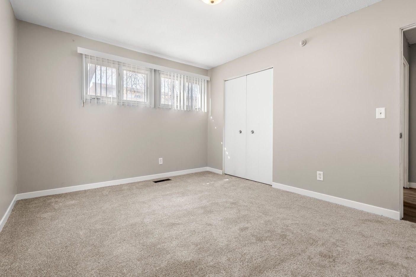 Empty beige bedroom with carpet, small windows, and white double closet doors