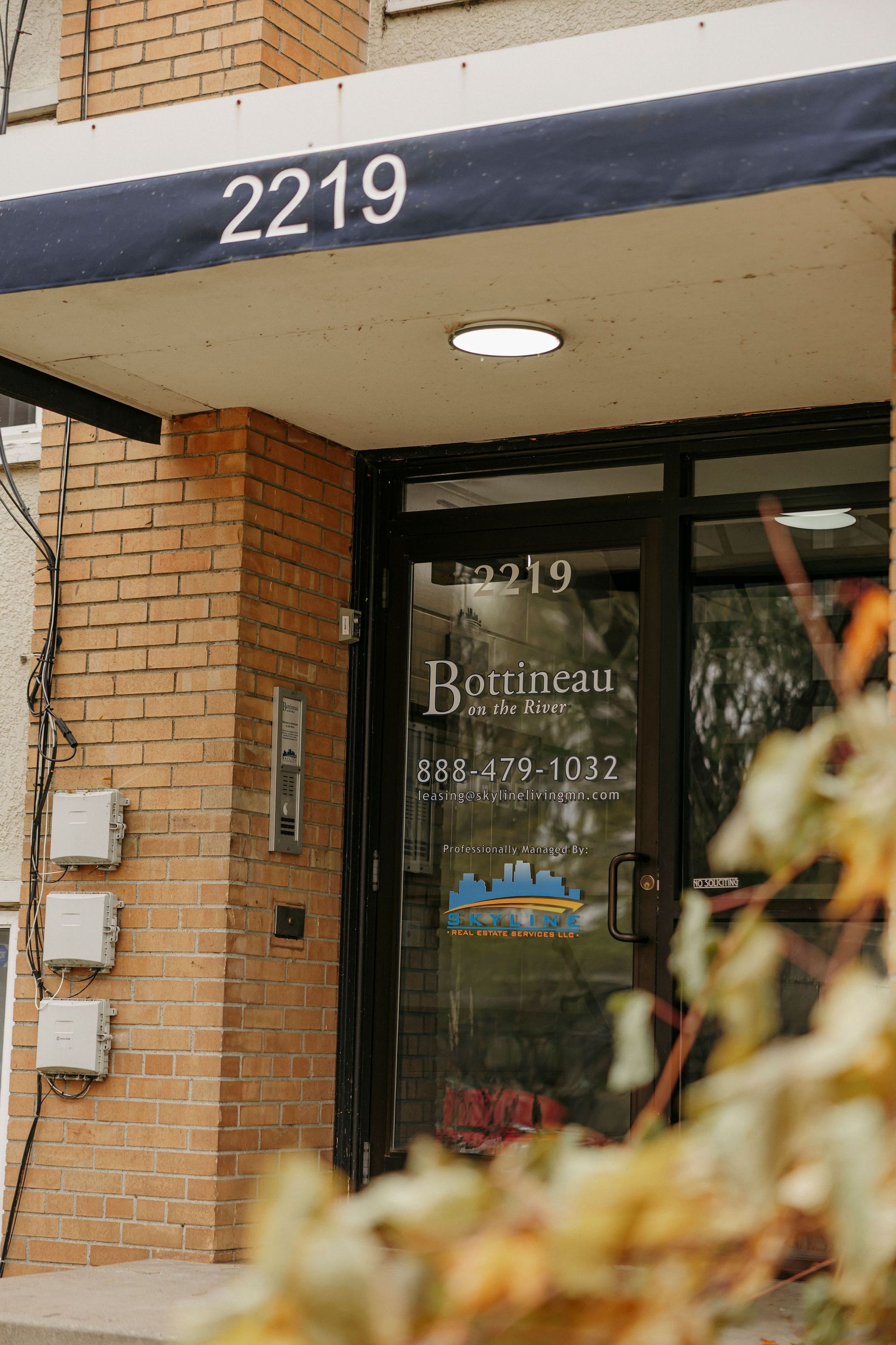 Entrance to a brick building with address 2219 and glass doors under a blue awning