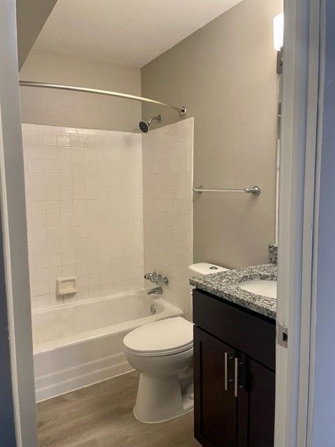Small bathroom with white tub, shower curtain, toilet, and dark vanity with granite countertop.