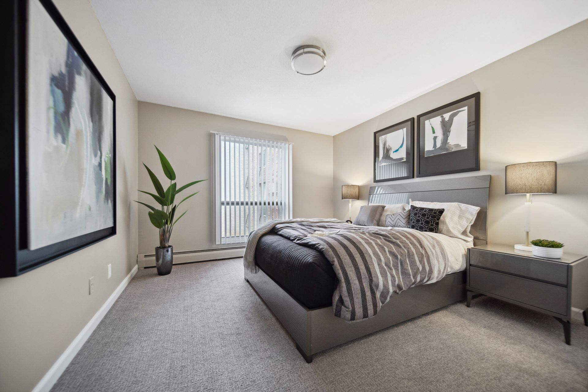 Bright modern bedroom with a bed, nightstand, lamp, plant, and abstract wall art