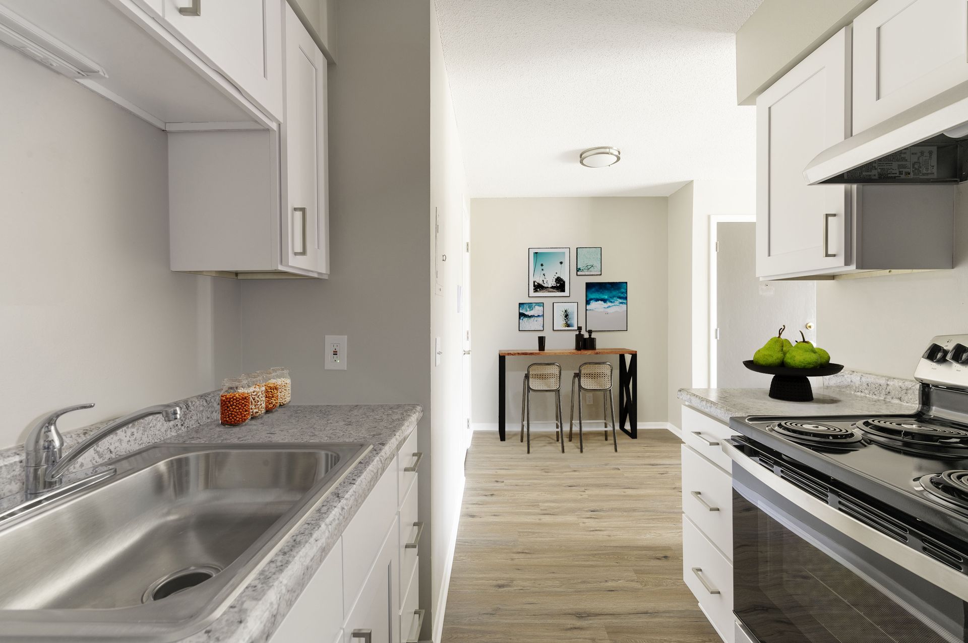 Bright white kitchen with stainless appliances, leading to a small dining area in the background