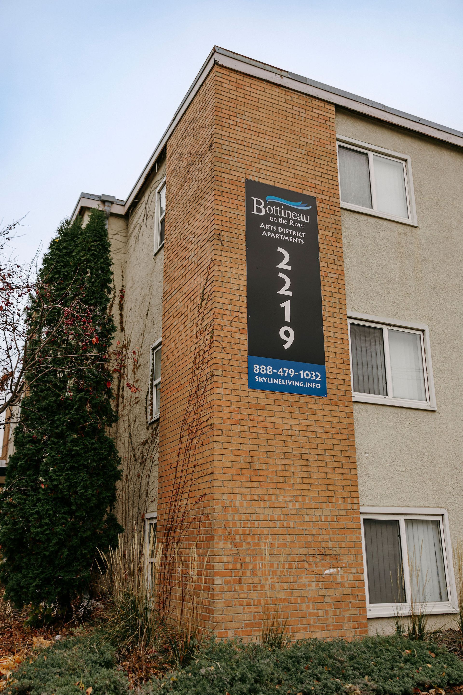 Brick apartment building with a vertical sign reading 2219 beside windows and ivy-covered wall