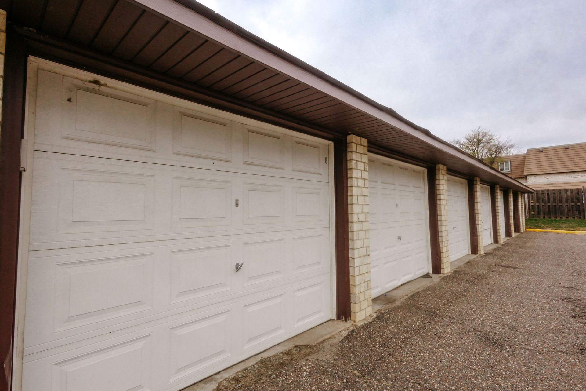 Row of white garage doors with brick pillars along a gravel driveway