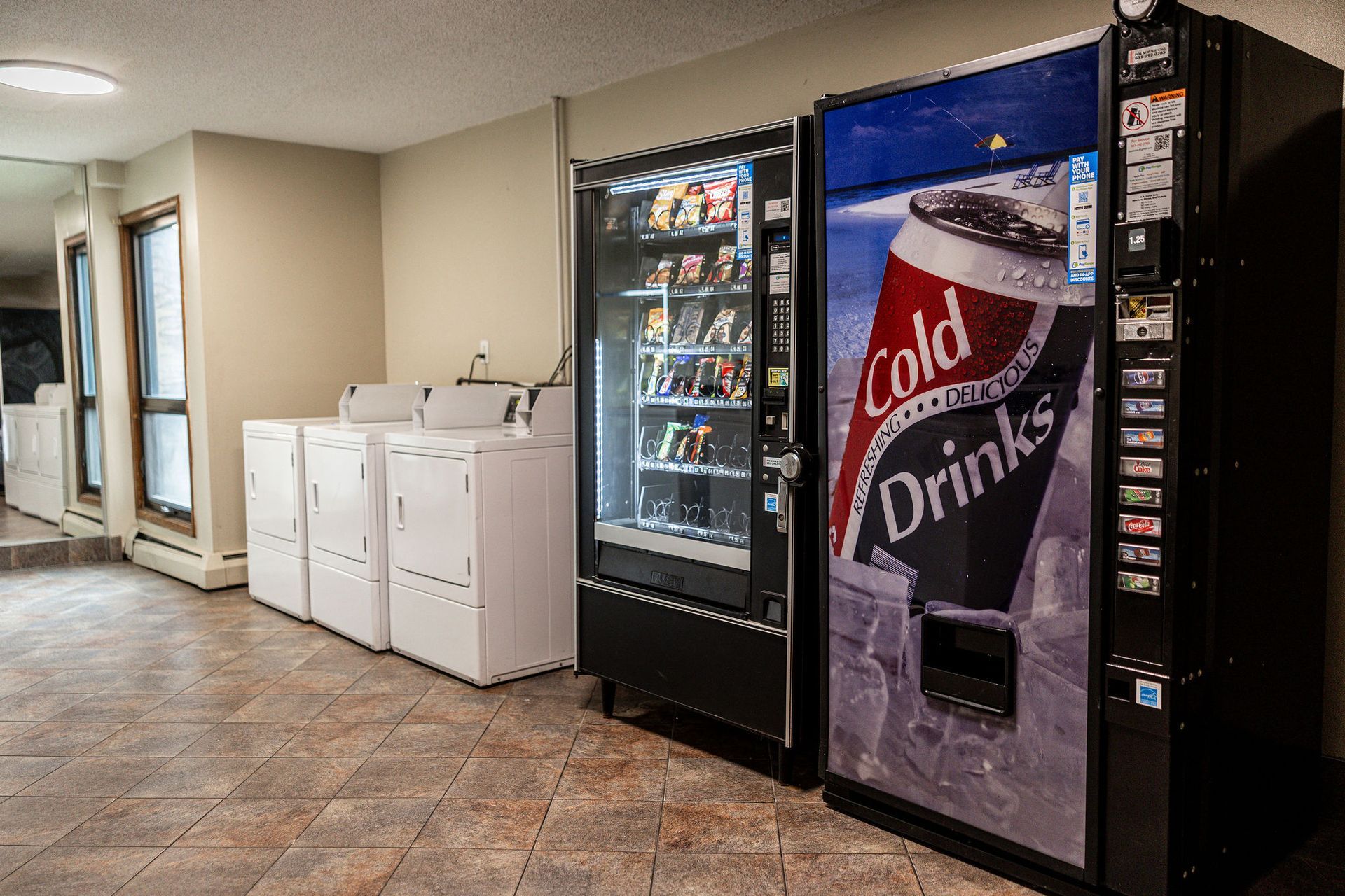 Hallway with laundry machines and two vending machines, including a soda machine and a snack machine.