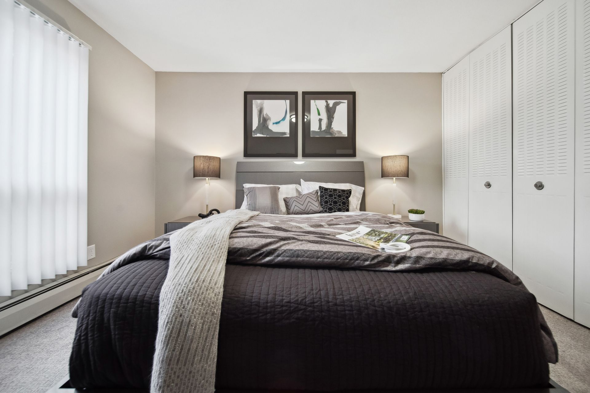 Bright bedroom with a dark bedspread, framed art above the bed, and white closet doors on the right