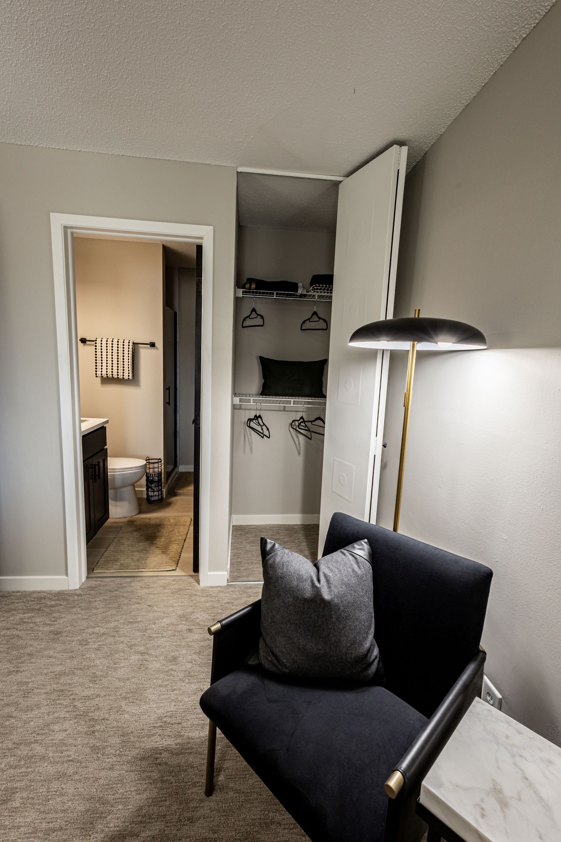Modern gray bedroom with chair, floor lamp, and open closet leading to a bathroom and bedroom beyond