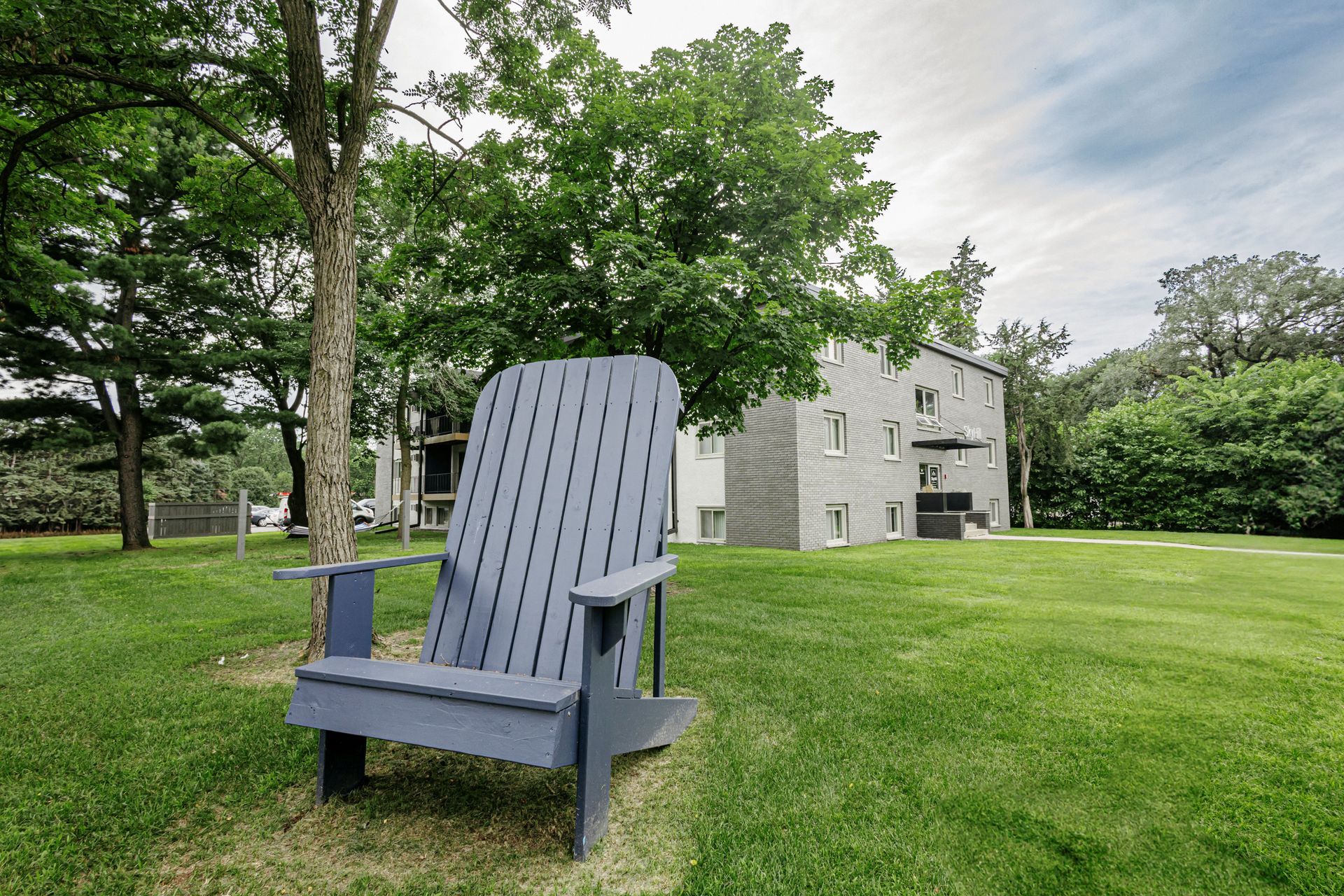 Blue Adirondack chair on a grassy lawn near trees and a white house