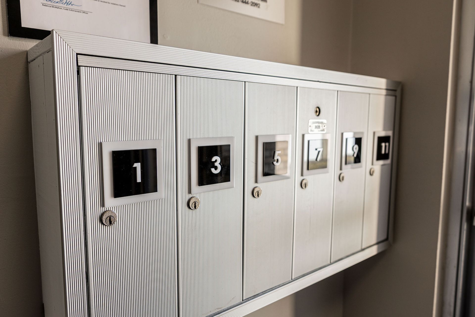 White wall-mounted mailbox unit with numbered slots and small mail icons in a hallway