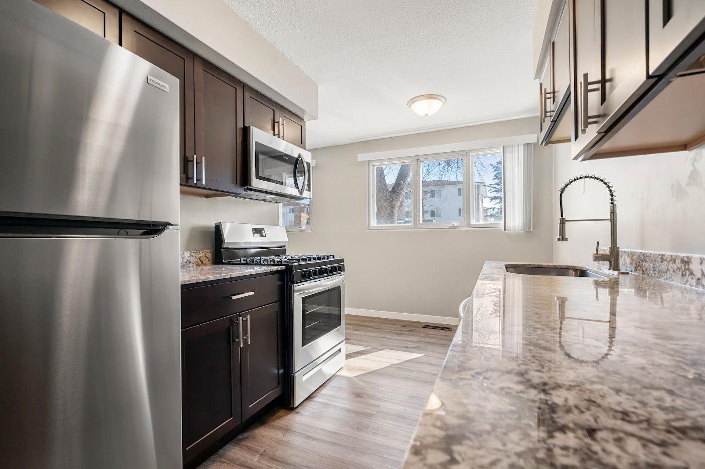 Bright modern kitchen with stainless steel appliances, dark cabinets, and a marble-look countertop.