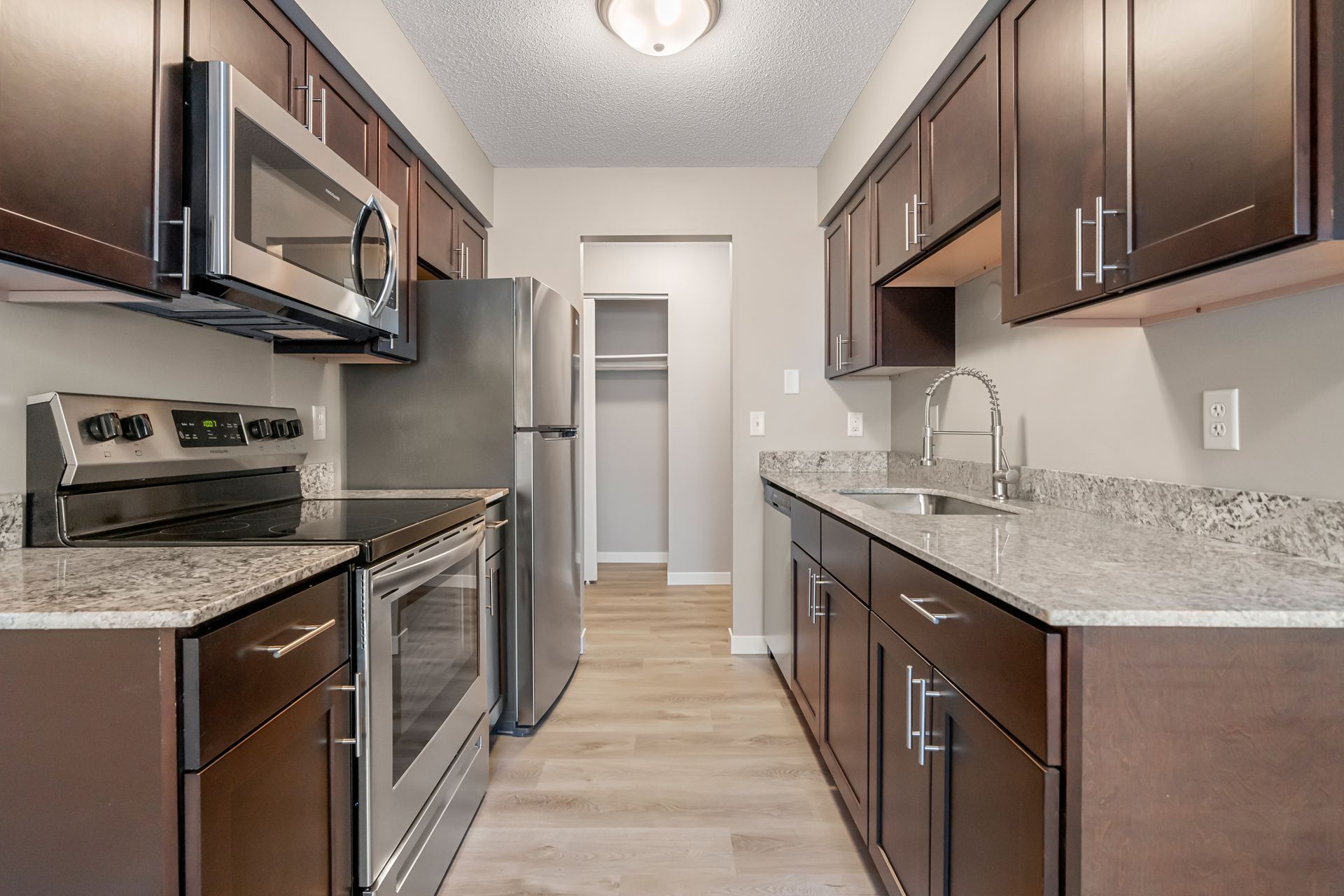 Modern kitchen with dark wood cabinets, stainless steel appliances, granite counters, and light wood flooring