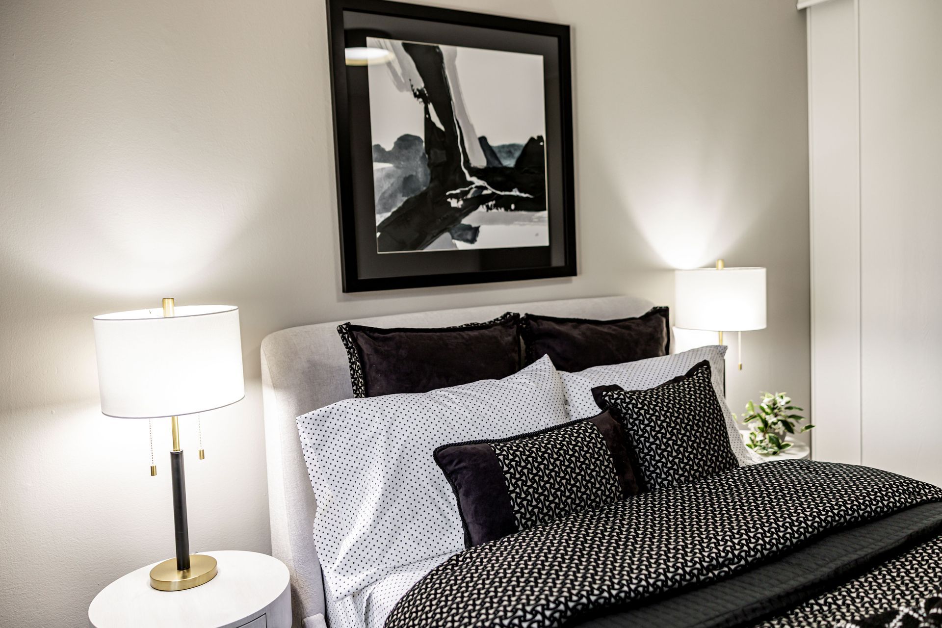 Neatly made bed with dark patterned bedding, white pillows, and bedside lamps in a softly lit bedroom.
