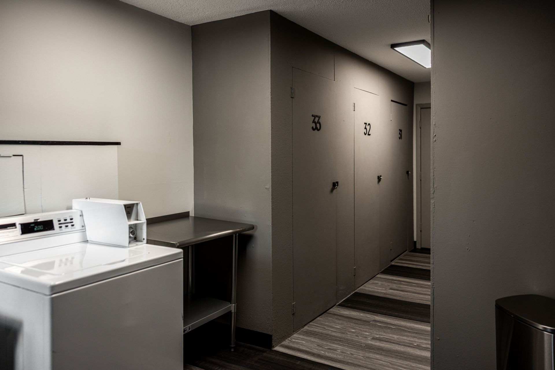 Laundry room with washer, sink, and row of lockers along a narrow hallway