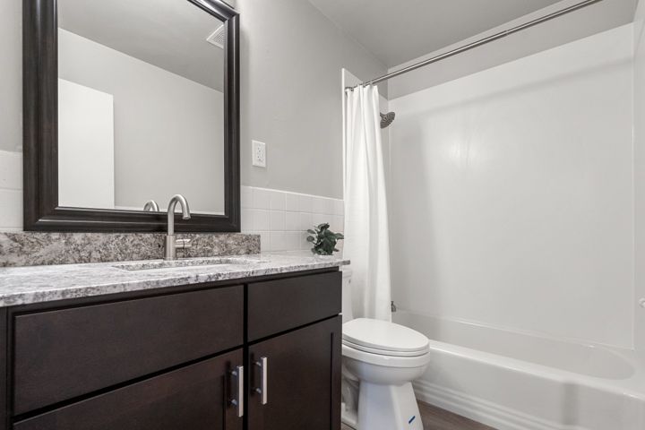 Small bathroom with dark vanity, mirror, sink, toilet, and white bathtub with shower curtain.