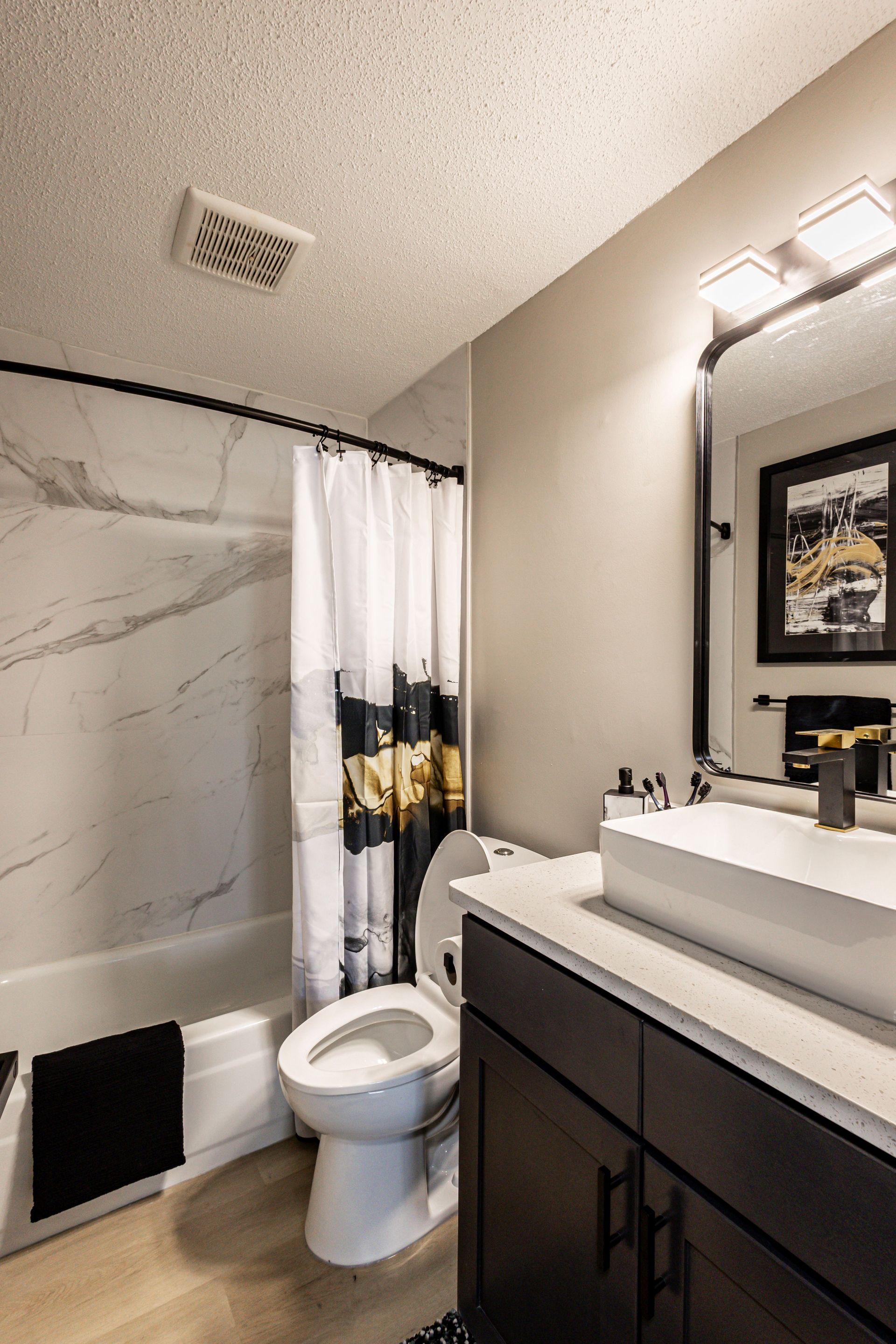 Modern bathroom with toilet, marble shower wall, dark vanity, and lit mirror above the sink