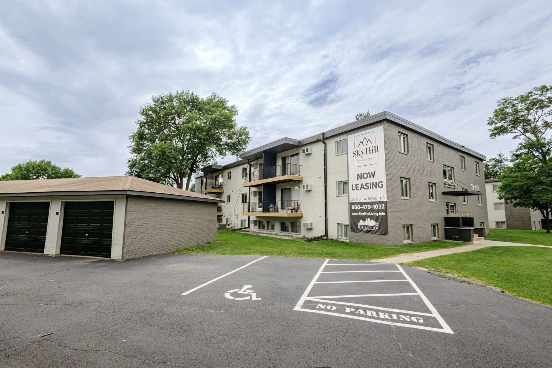 Apartment building with garages, parking lot, and grass under a cloudy sky