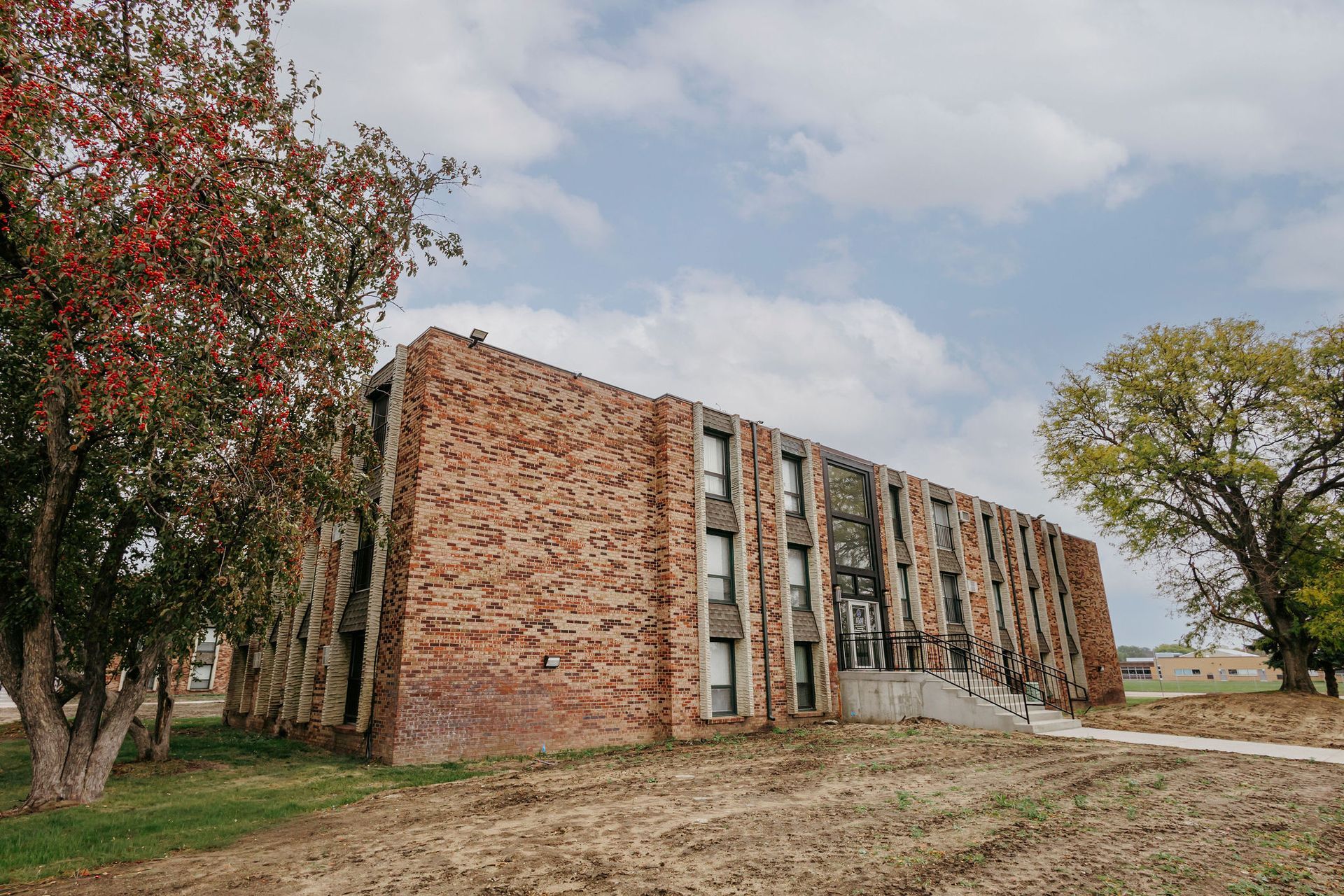 Brick apartment building with narrow windows beside trees under a partly cloudy sky