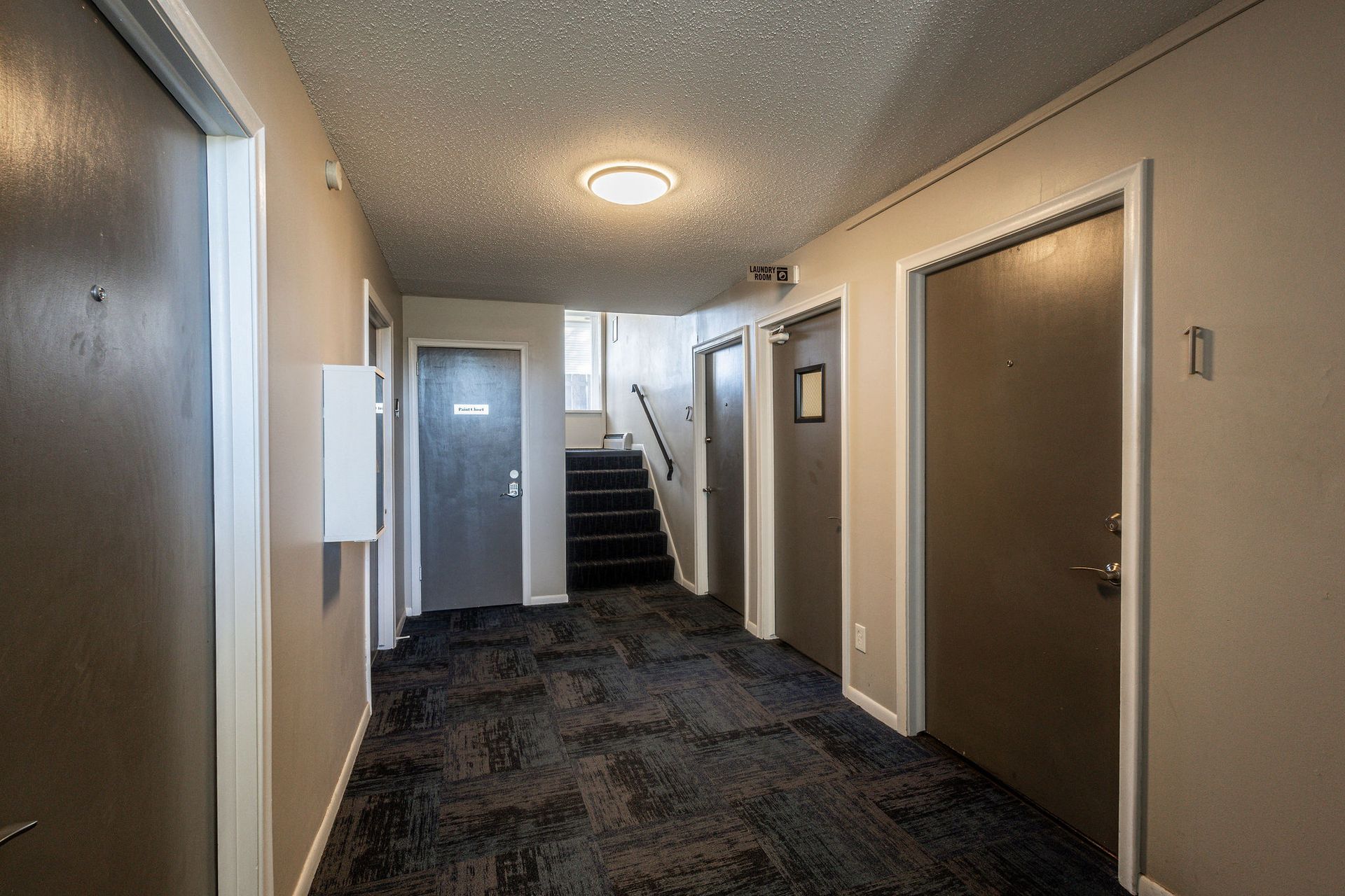 Apartment hallway with carpet, closed doors, and stairs at the end