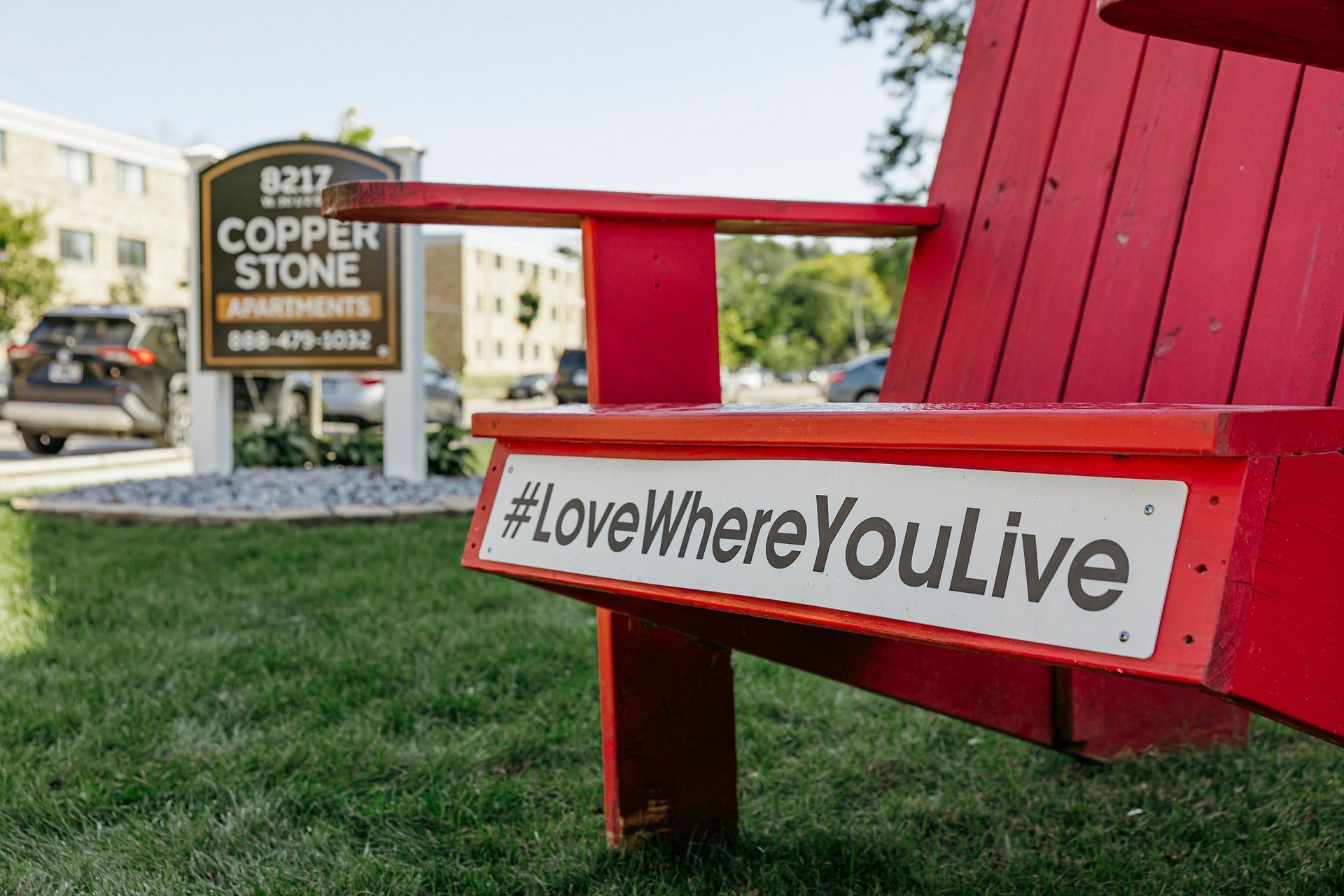 Red bench with #LoveWhereYouLive sign outside Copper Stone apartments