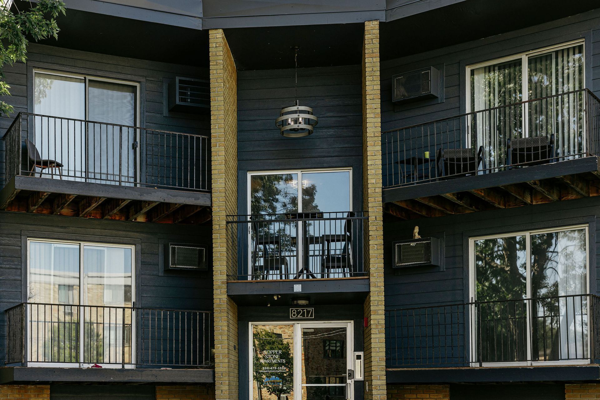 Apartment building facade with balconies, dark siding, and white-trimmed windows in daylight