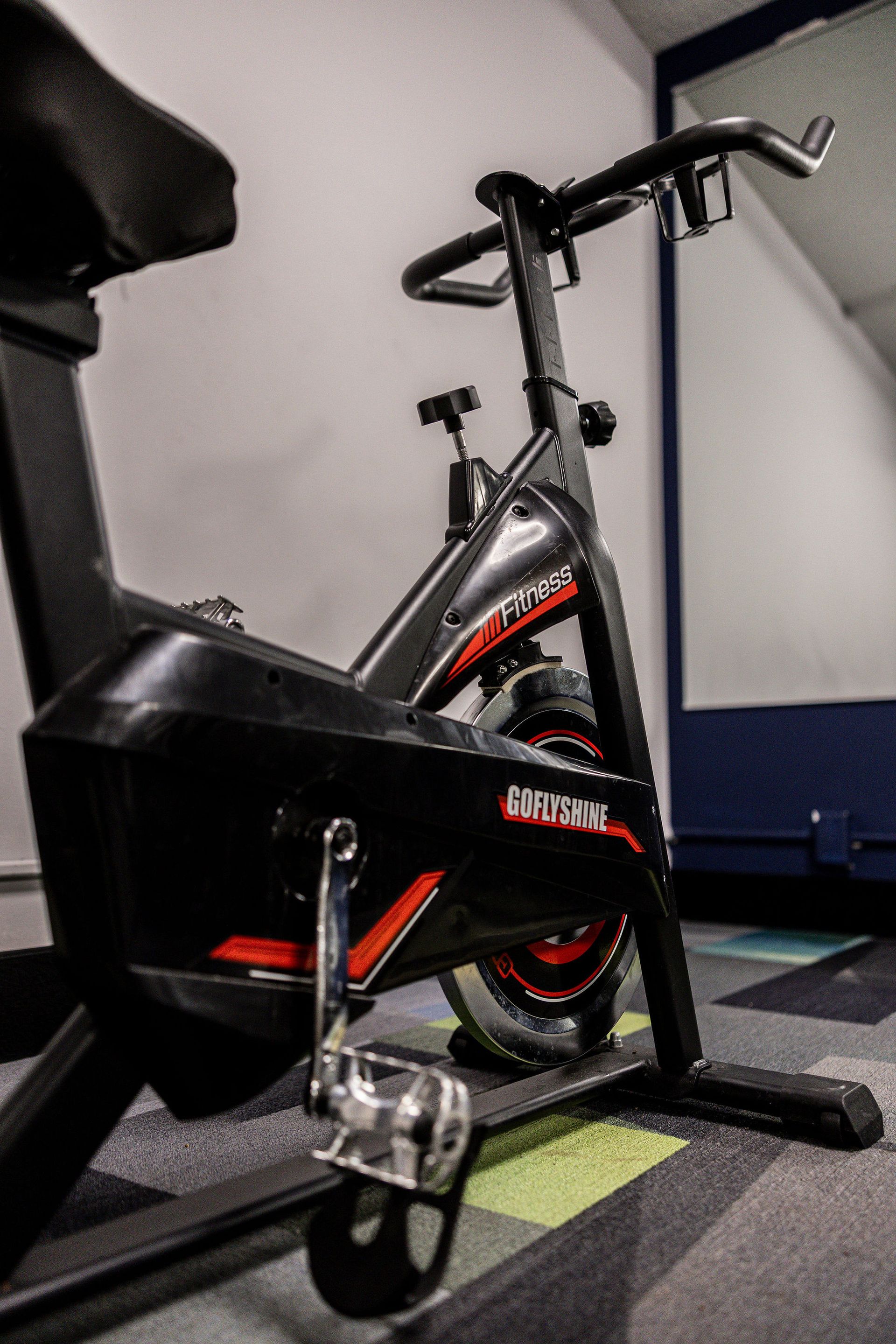 Black stationary exercise bike in a gym corner, with red accents and a black saddle.