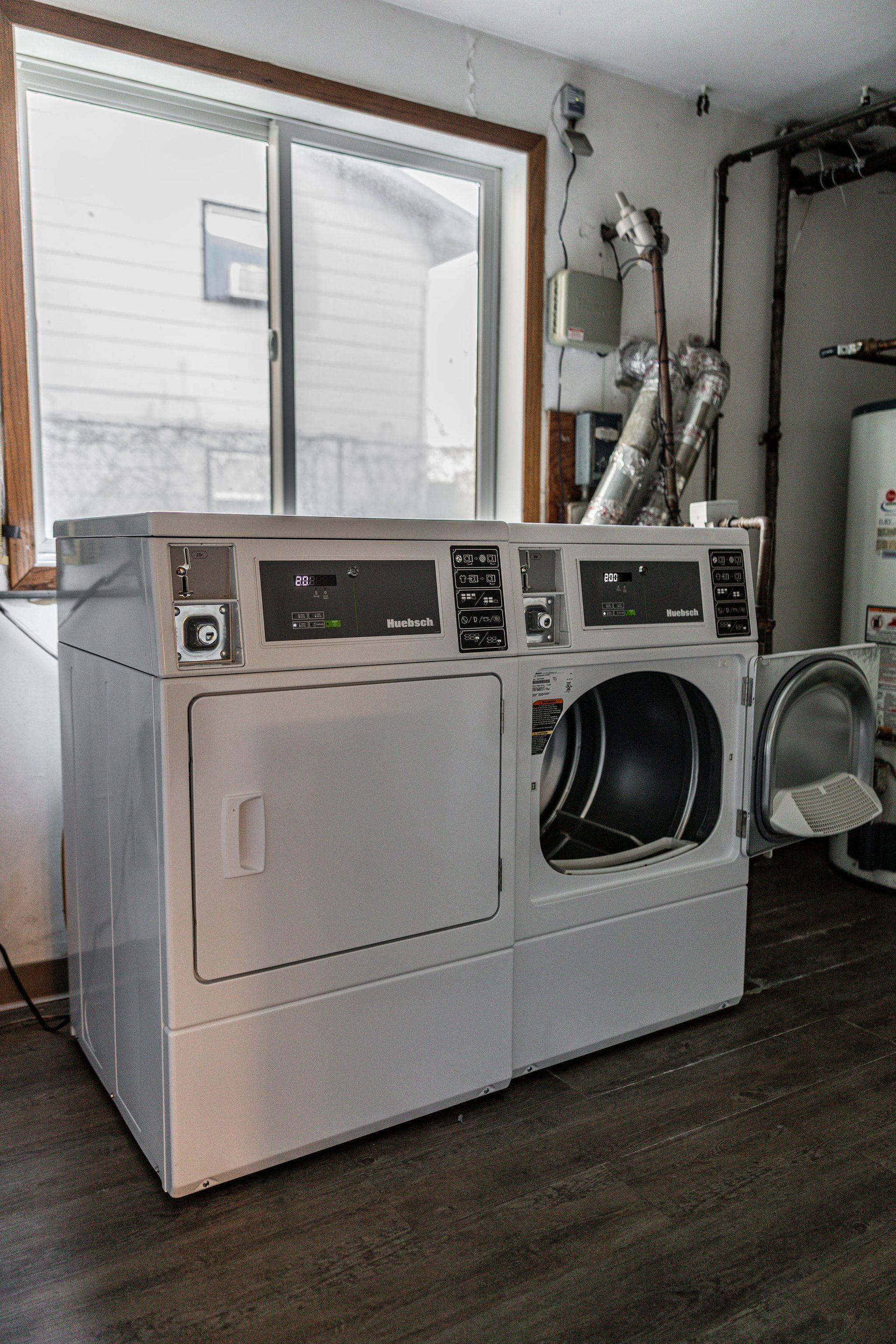 Laundry room with a white washer and dryer under a window, plus exposed vent ducting on the right.