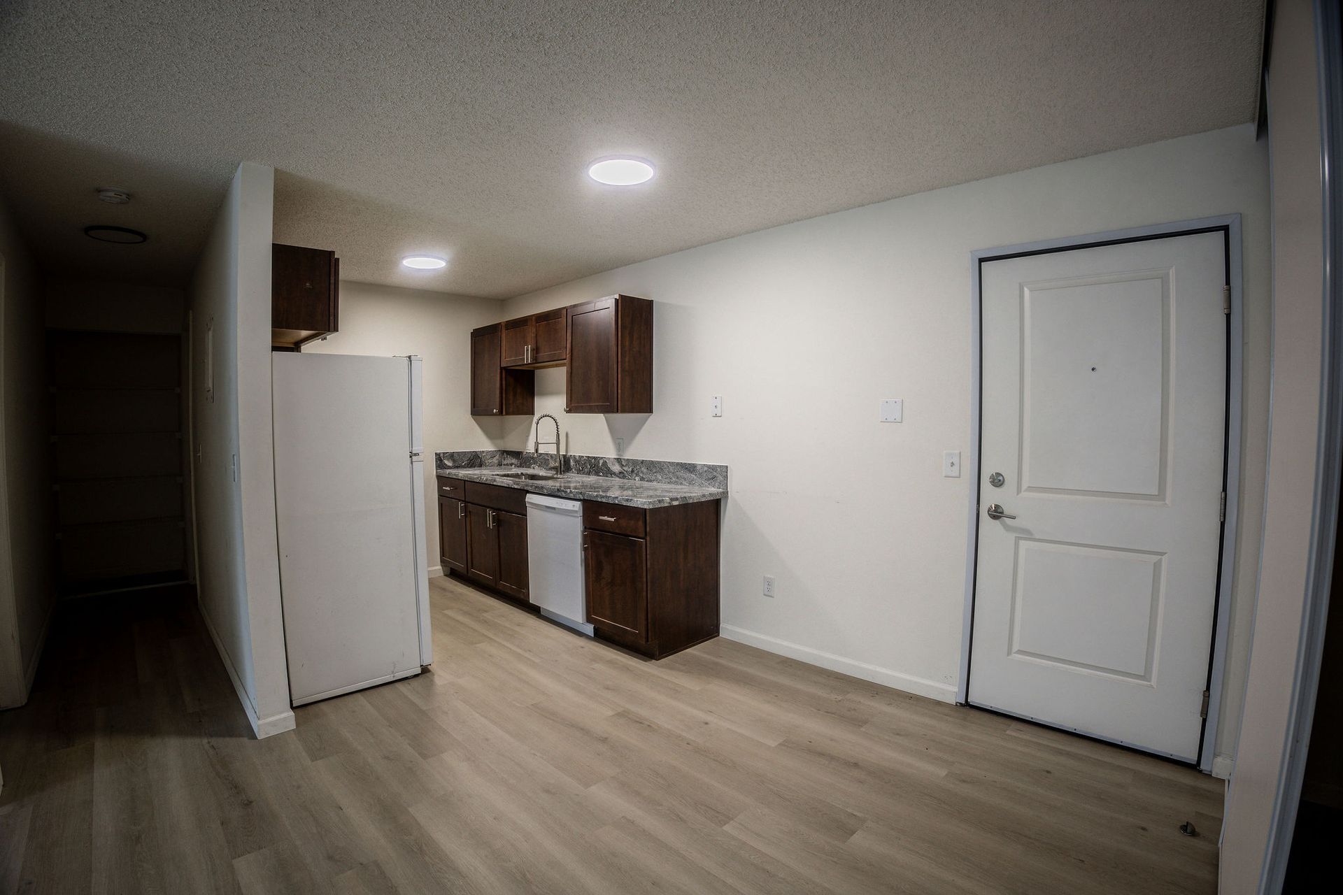 Empty apartment kitchen with white fridge, dark cabinets, and a closed white door