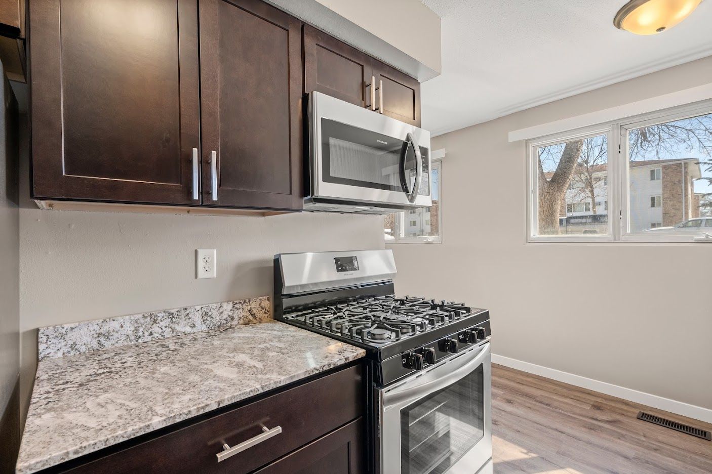 Small modern kitchen with dark cabinets, granite counters, gas stove, microwave, and window light